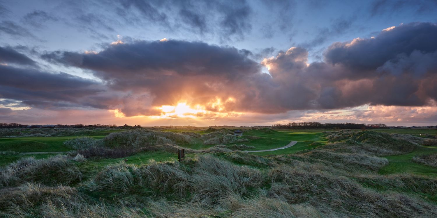 Dramatic sunset over links golf course with rolling dunes and vibrant orange sky.