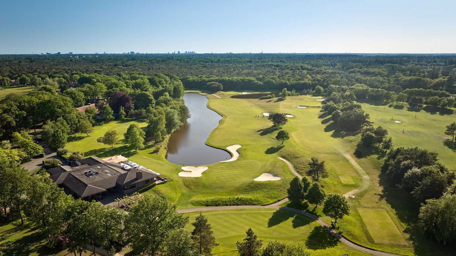 Aerial view of a golf clubhouse beside a lake on a sunny green golf course.