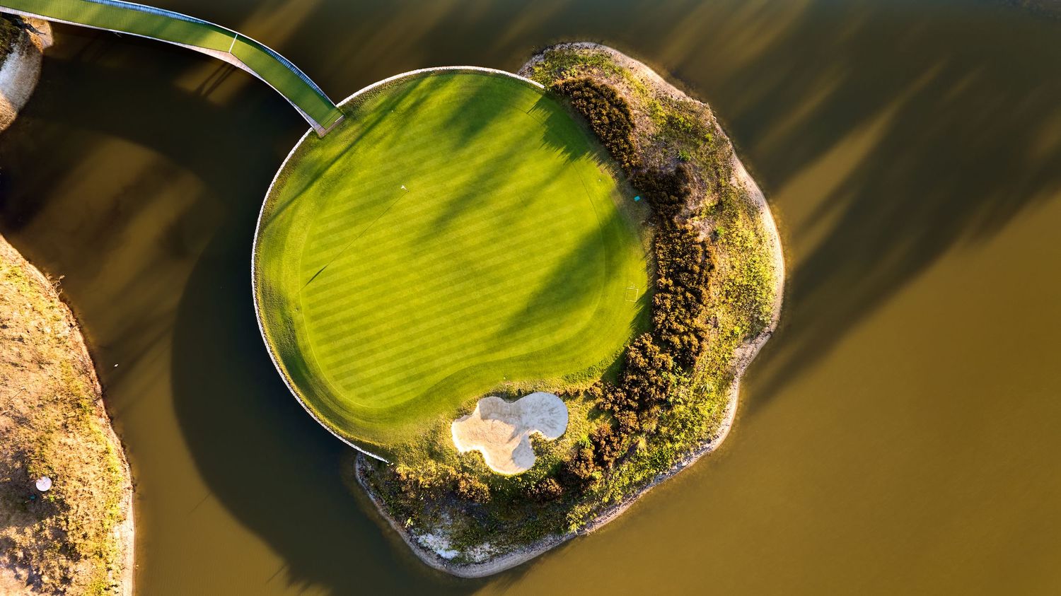 Aerial top-down view of an island golf green surrounded by water with a single flag pin.