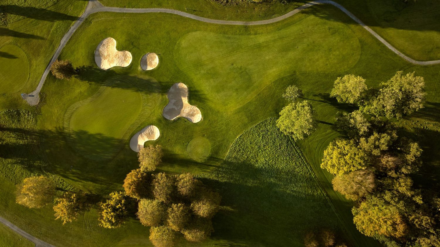Aerial drone view of golf course with multiple sand bunkers, green fairways, and surrounding trees.