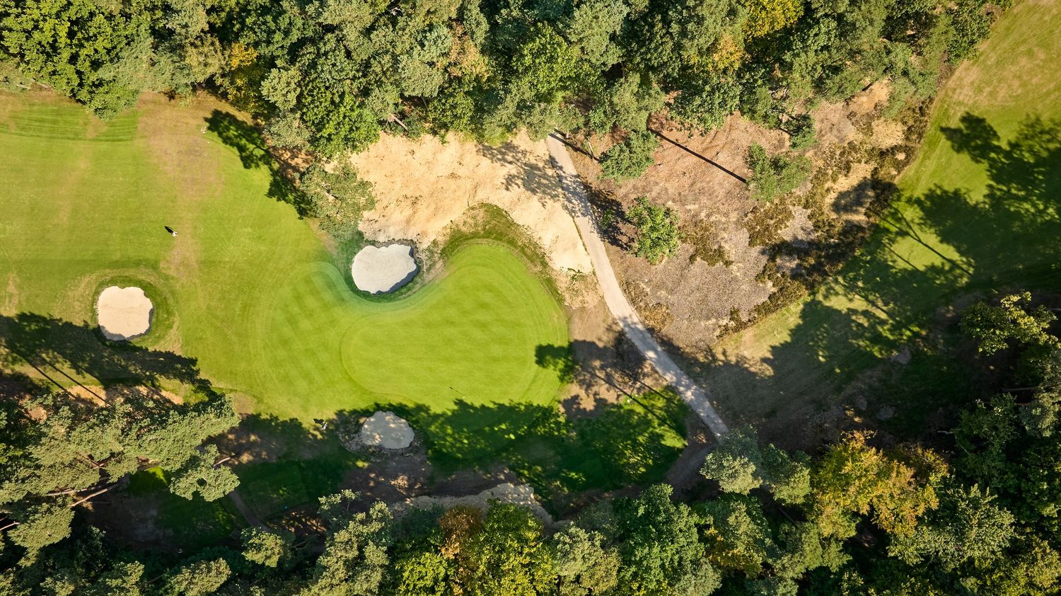 Top-down aerial view of a golf green surrounded by dense trees, sand bunkers, and a winding stream.
