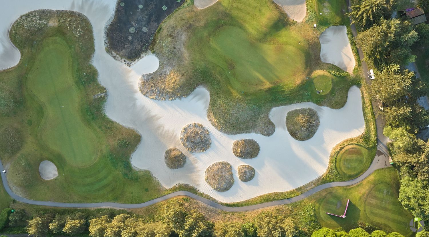 Top-down aerial view of a golf course featuring large white sand bunkers surrounded by green fairways and water.