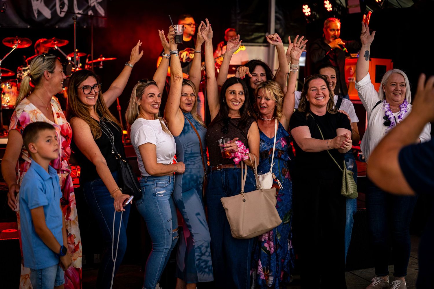 Group of happy women cheering and raising hands at a lively indoor concert event.