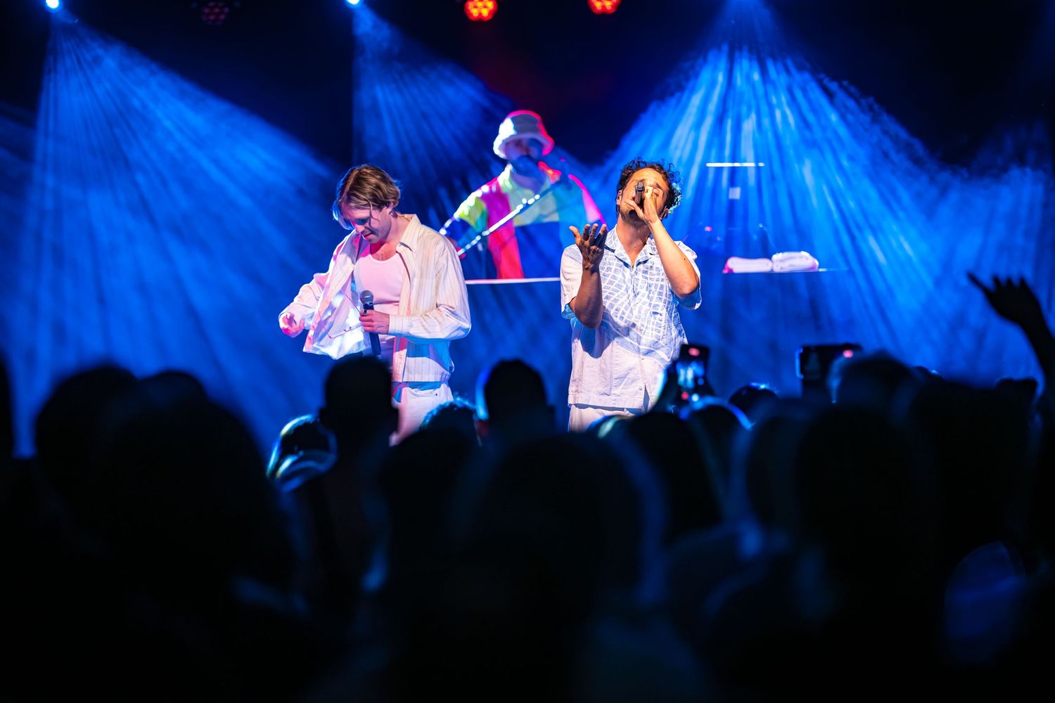 Two performers sing on stage under blue lights at a live concert with an enthusiastic crowd.