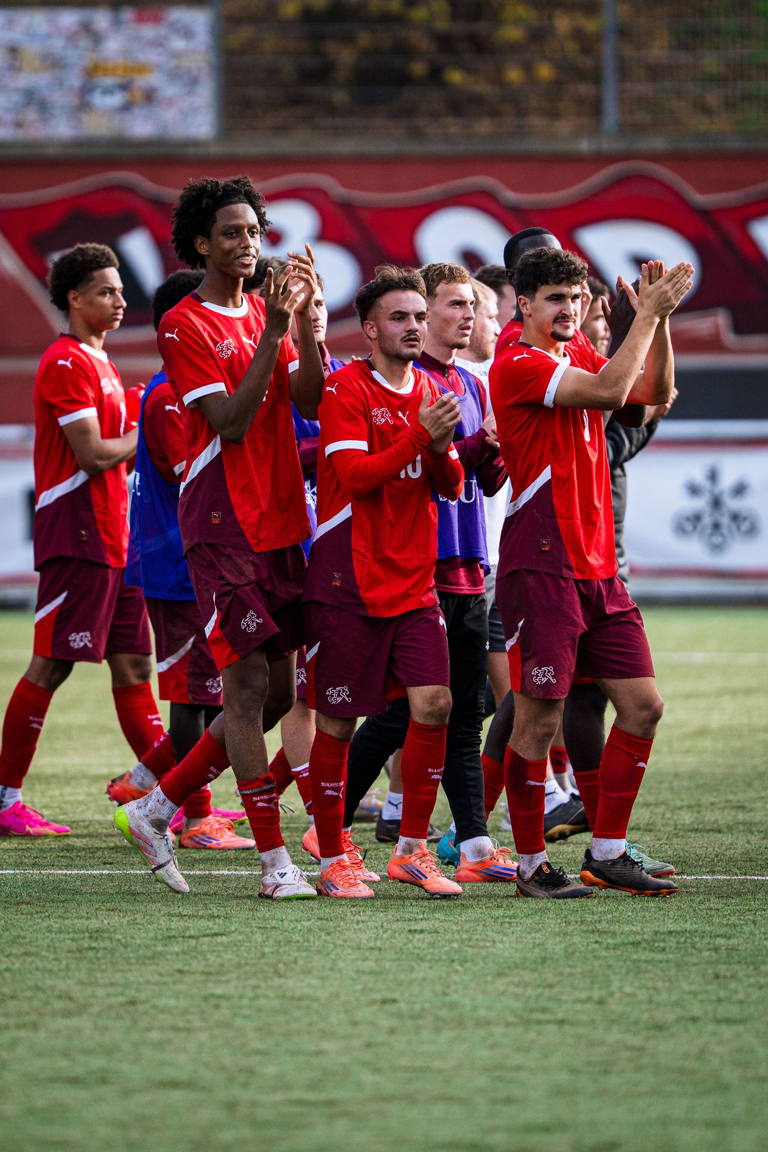 Soccer team in red uniforms applauding fans after a match on a green field.