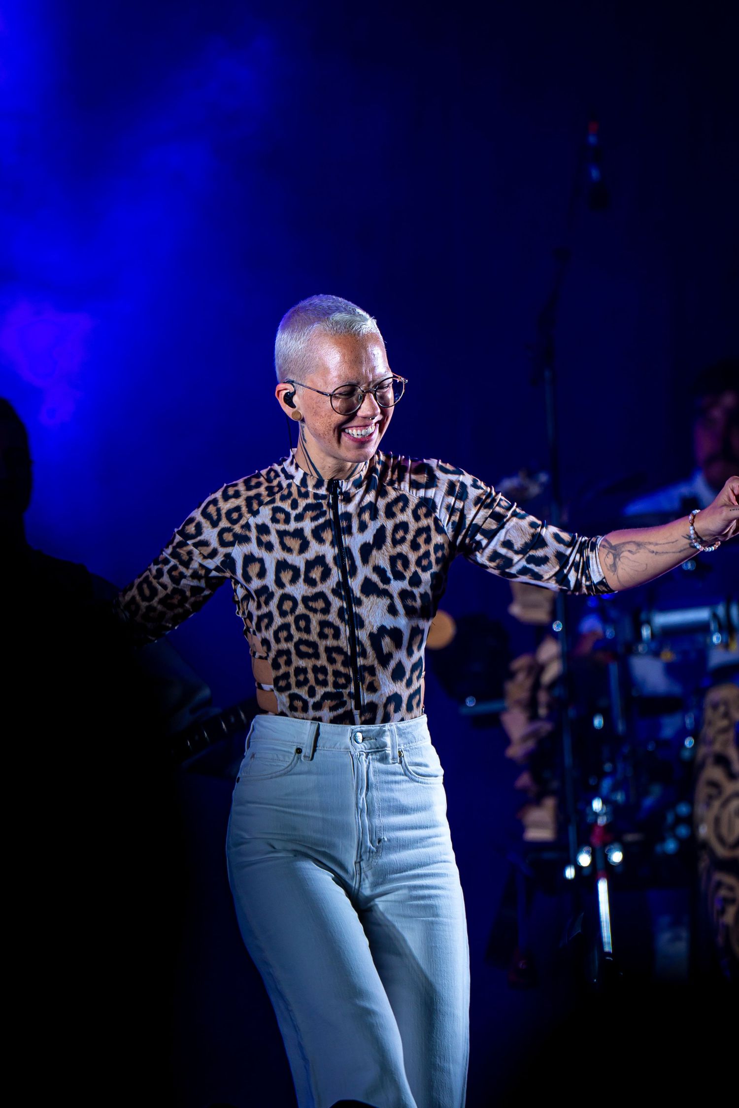 Performer in leopard print shirt and white jeans dancing on stage under blue lights.