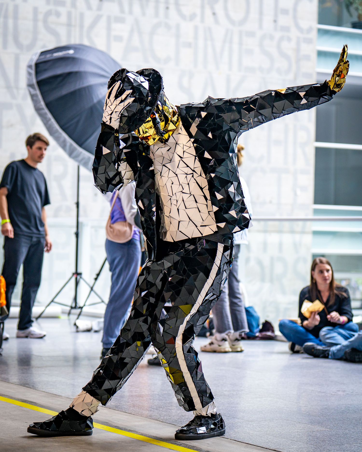 A performer in a geometric mirrored Michael Jackson costume strikes a dramatic dance pose at an indoor event.
