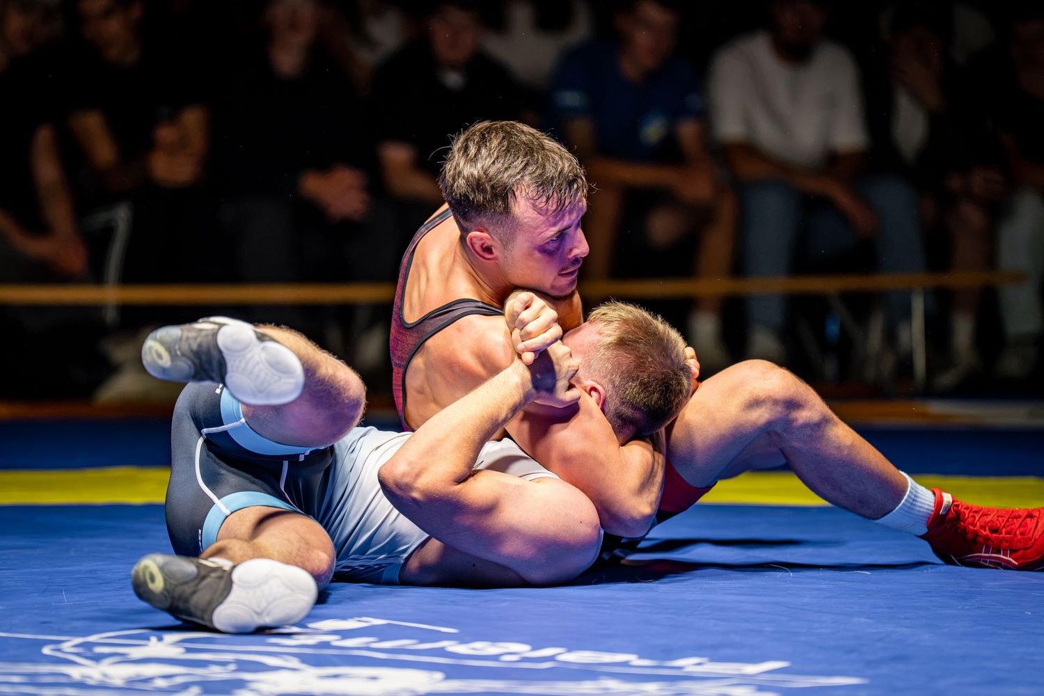 Two wrestlers compete on a mat, with one athlete pinning the other down during an intense wrestling match.