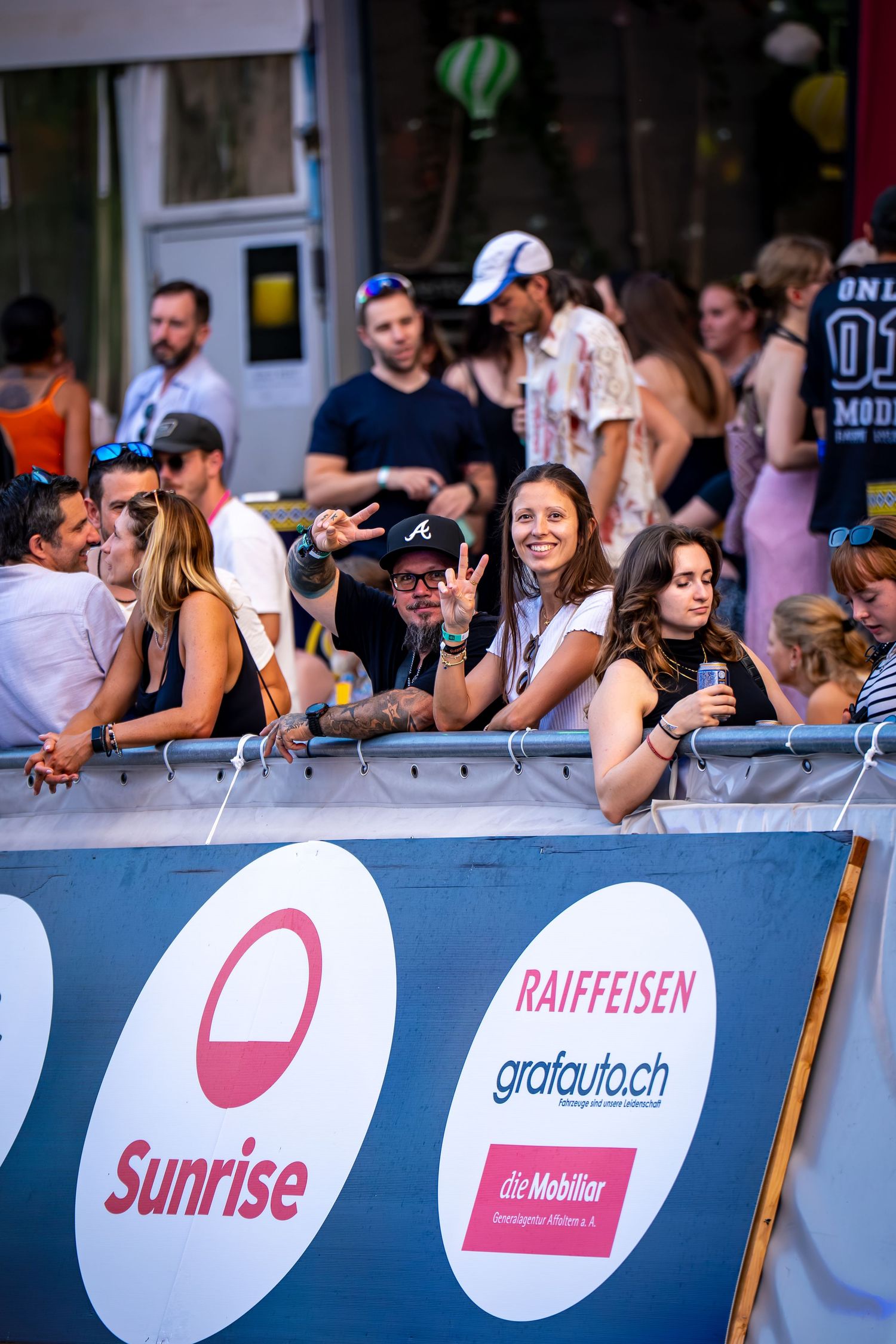 Crowd of festival-goers leaning on a barrier with Sunrise and Raiffeisen sponsor banners at an outdoor event.