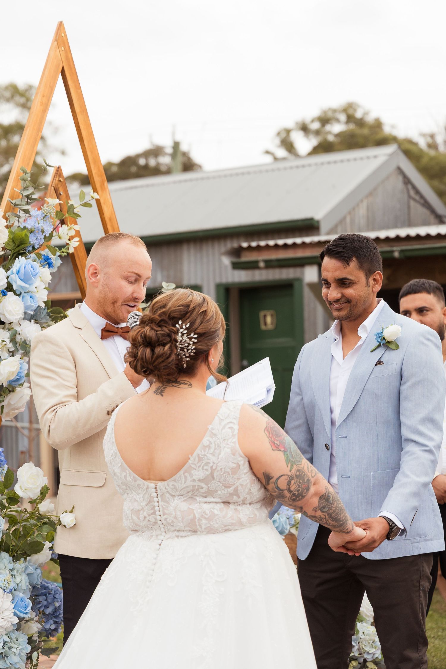 Bride and groom exchanging vows outdoors at a rustic wedding ceremony with blue floral arch decorations.