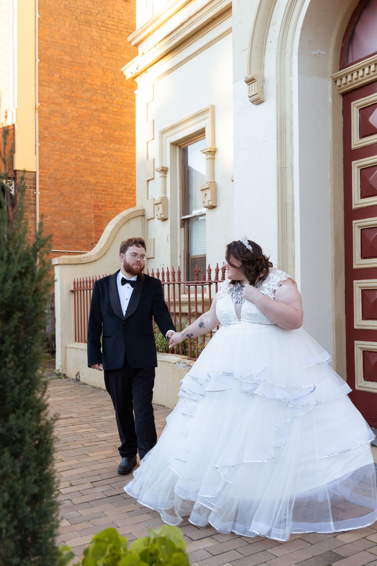 Bride and groom walk hand in hand along a brick pathway beside a classic heritage building.