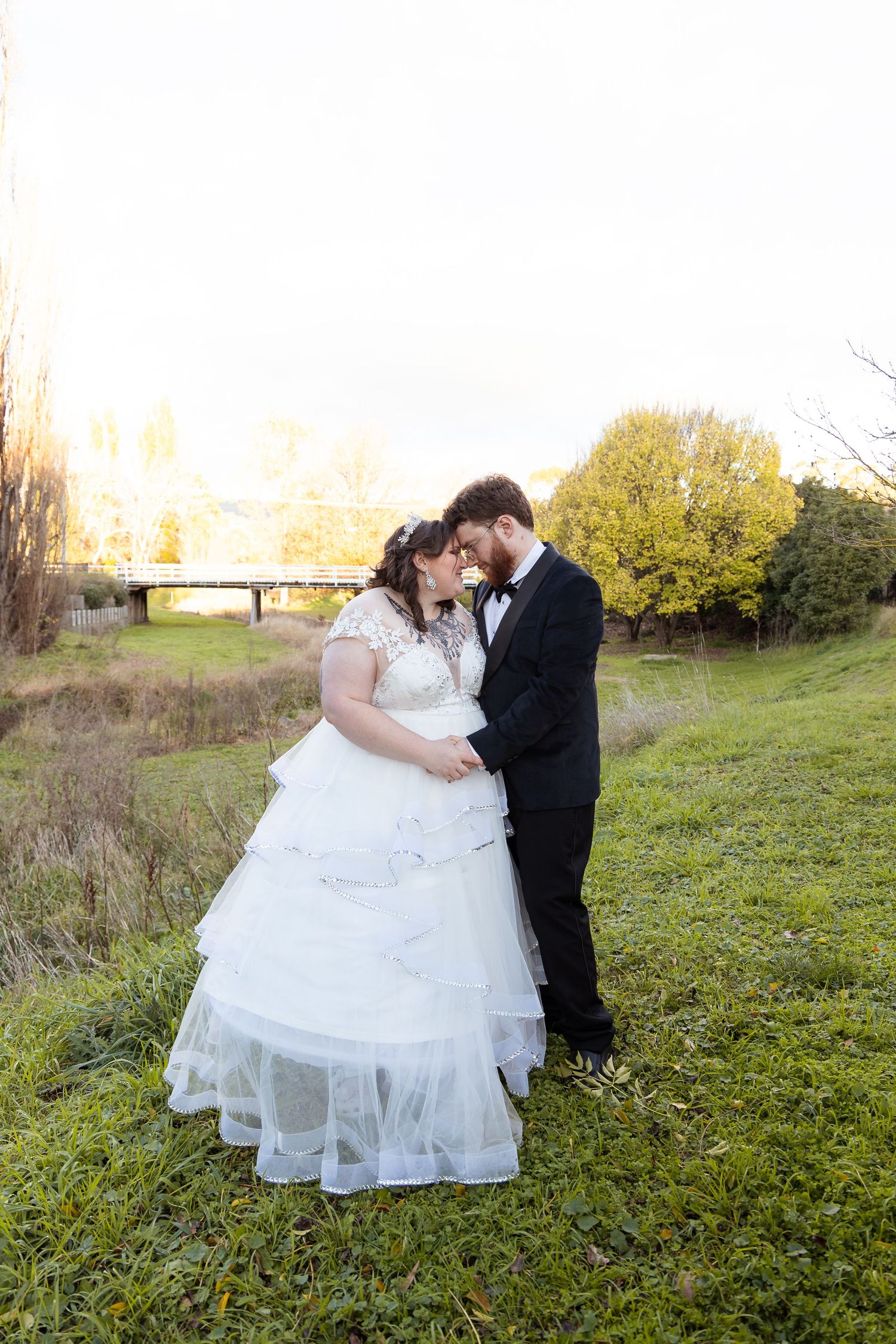 Bride and groom share an intimate forehead touch at sunset beside a peaceful green countryside.