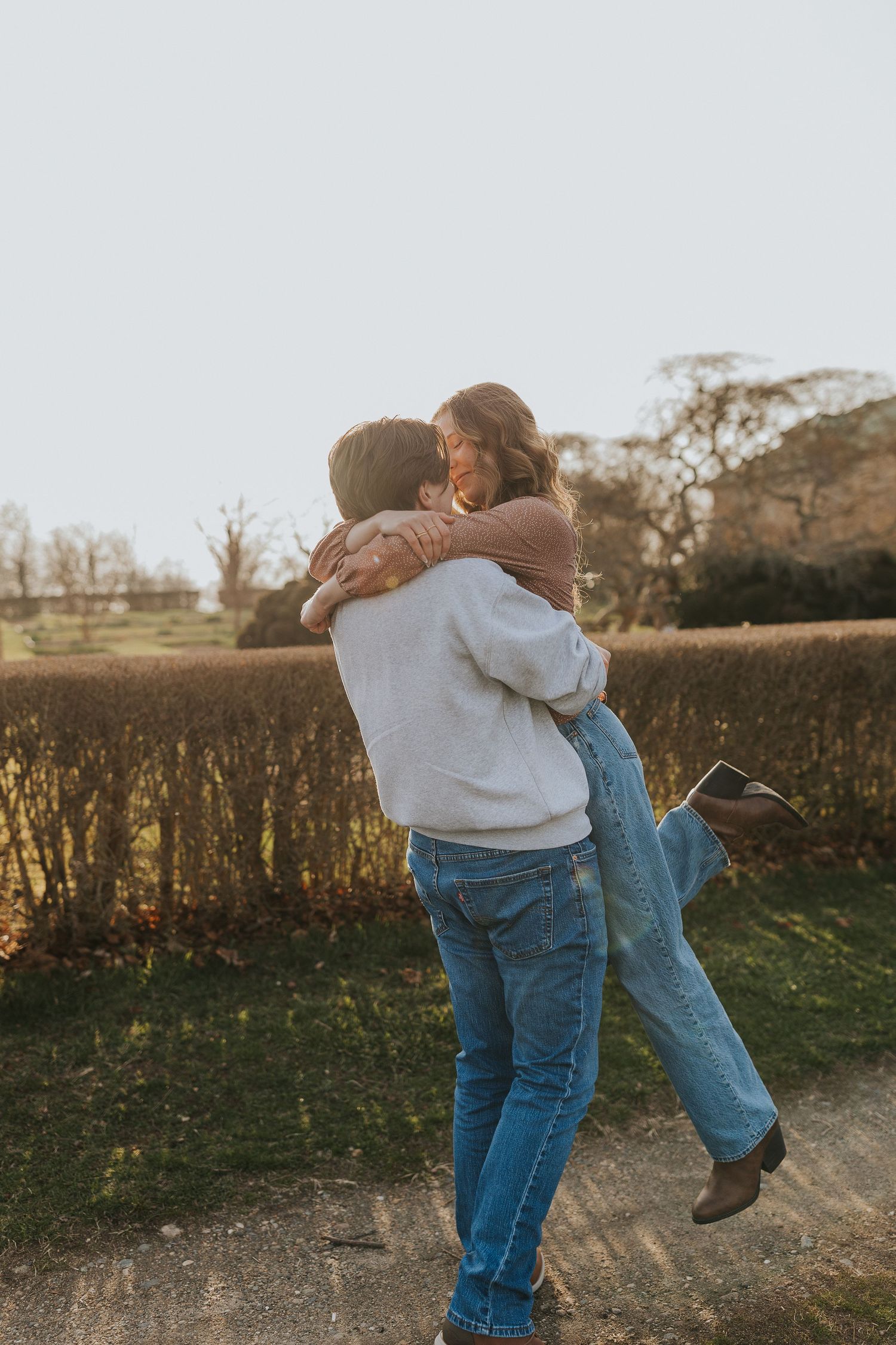 Man lifts and spins woman joyfully during a romantic outdoor couples engagement photo session.