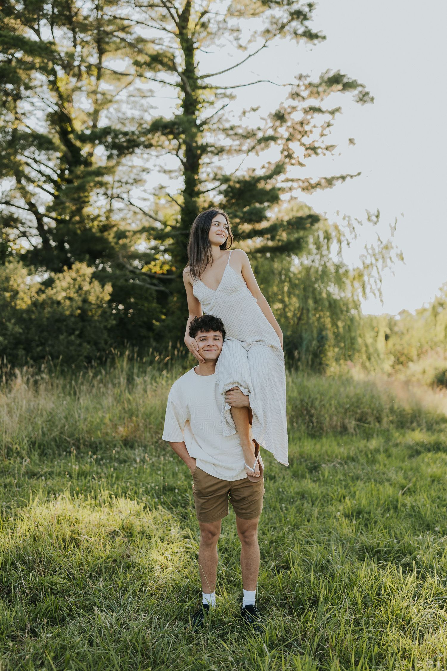 Romantic couple in a sunny meadow, woman in white dress lifted by man in casual attire.