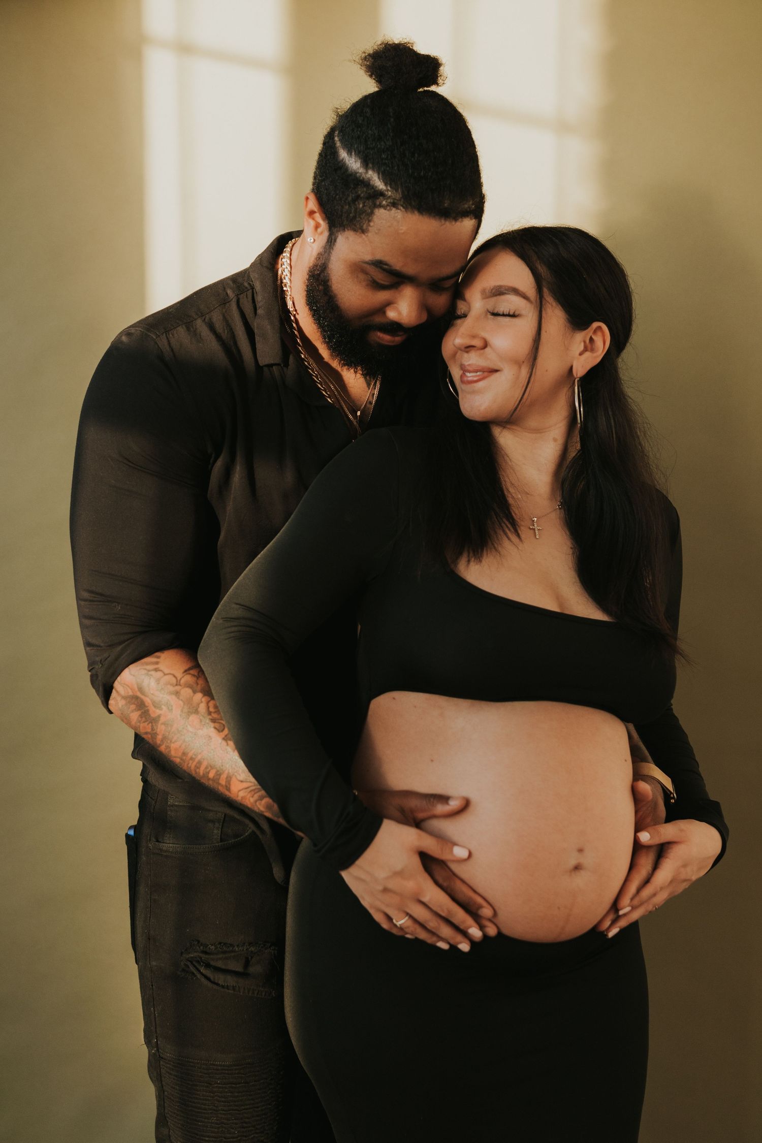 Man in black shirt embracing pregnant woman from behind, both cradling her baby bump.