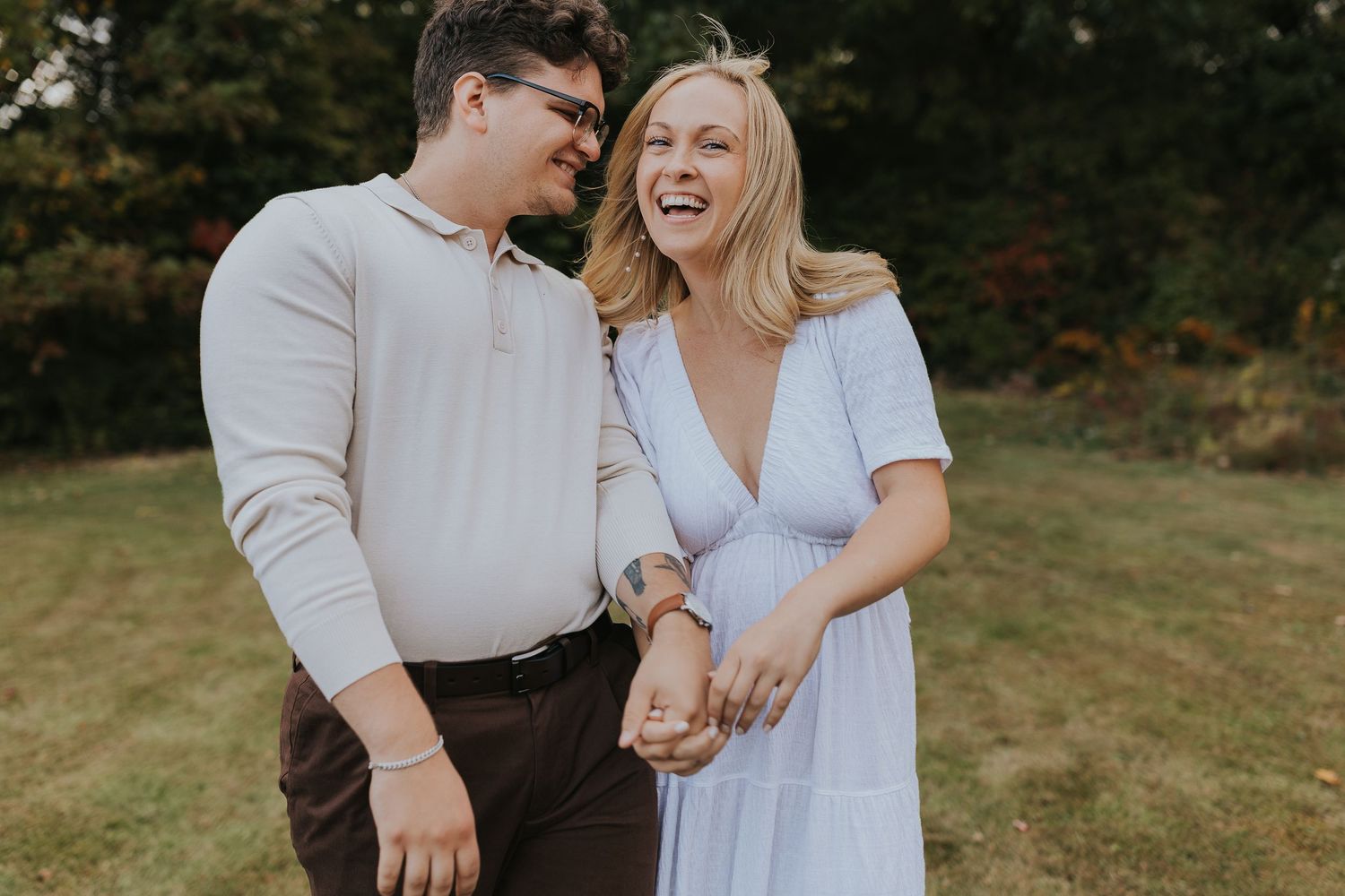 Happy couple laughing together outdoors during fall engagement photo session in a green field.