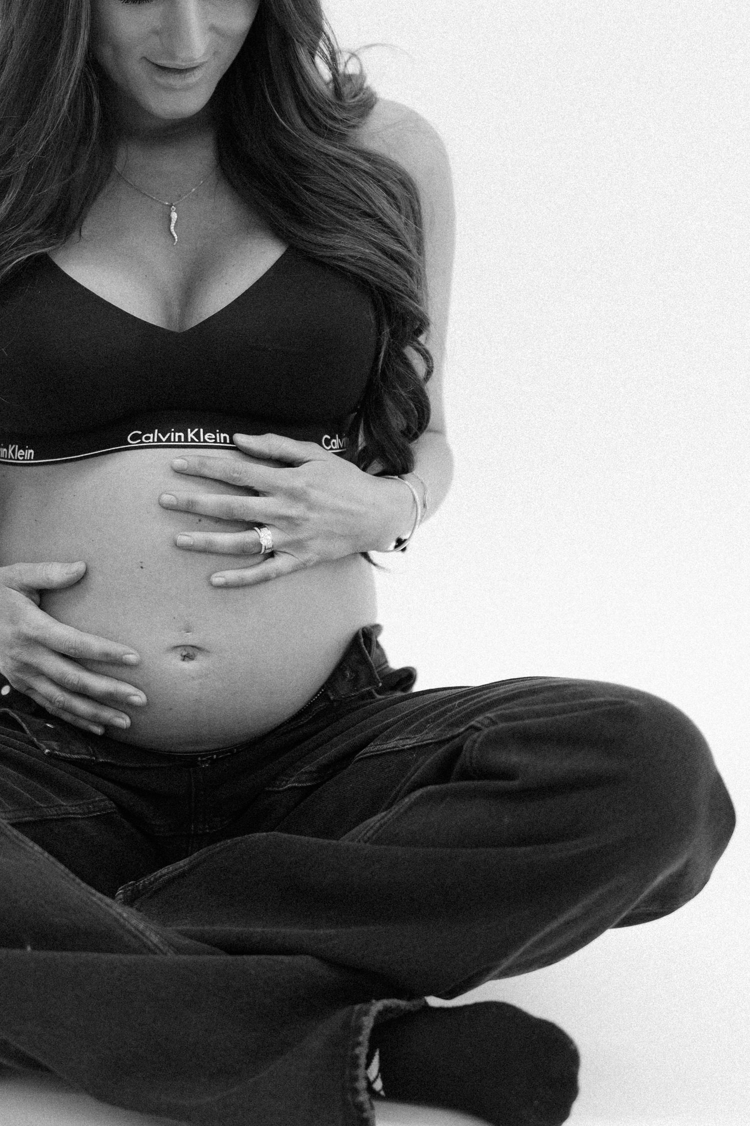 Close-up black and white photo of pregnant woman in Calvin Klein bralette cradling baby bump.