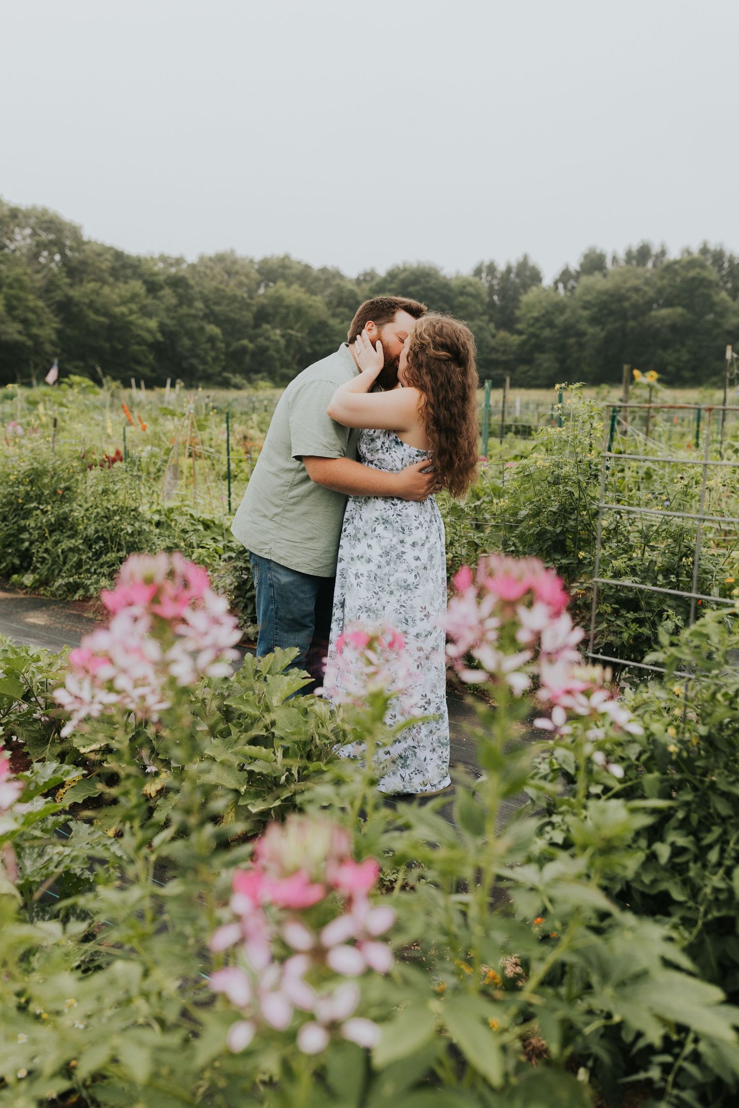 Couple sharing a passionate kiss surrounded by blooming flowers and lush greenery in a garden setting.