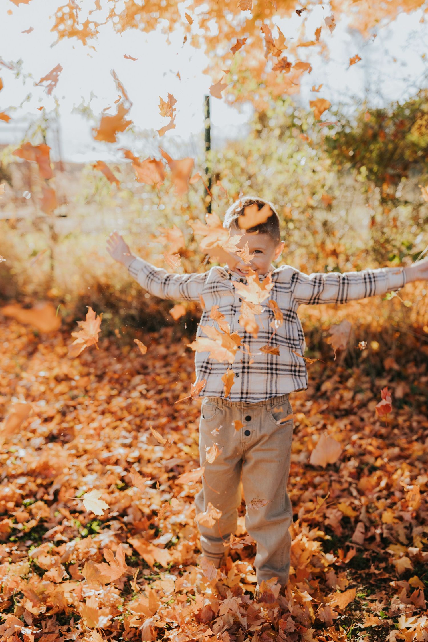 A young boy joyfully tosses golden autumn leaves in the air outdoors during fall.