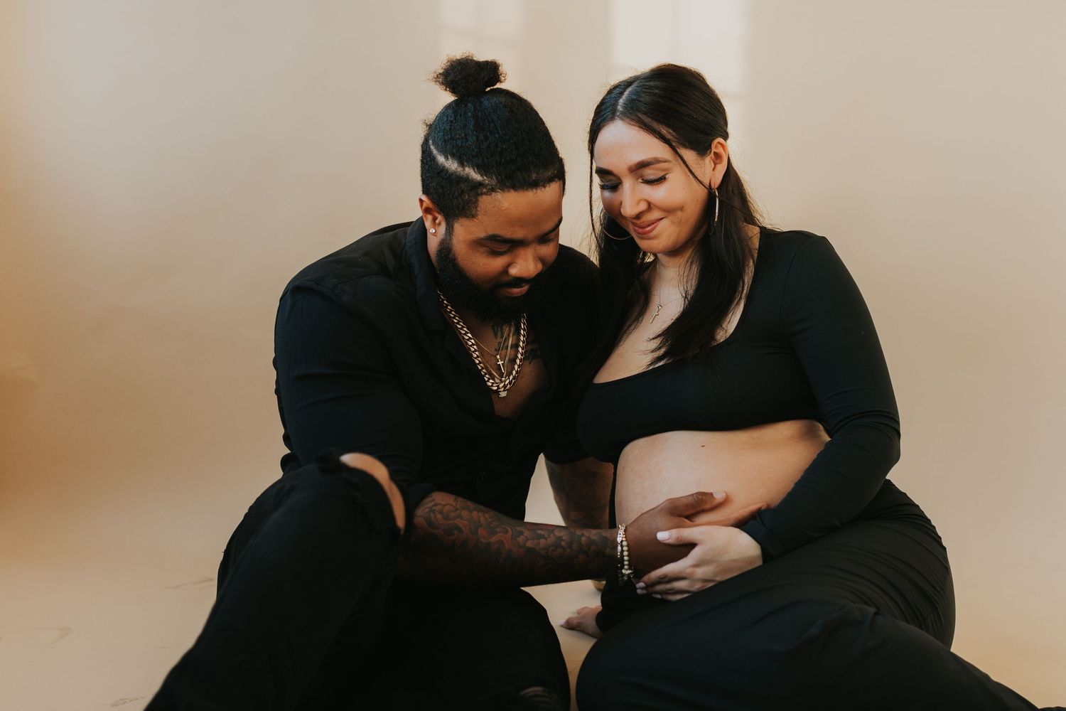 Couple in black outfits sharing a tender maternity moment, man gently touching pregnant woman's bare belly.