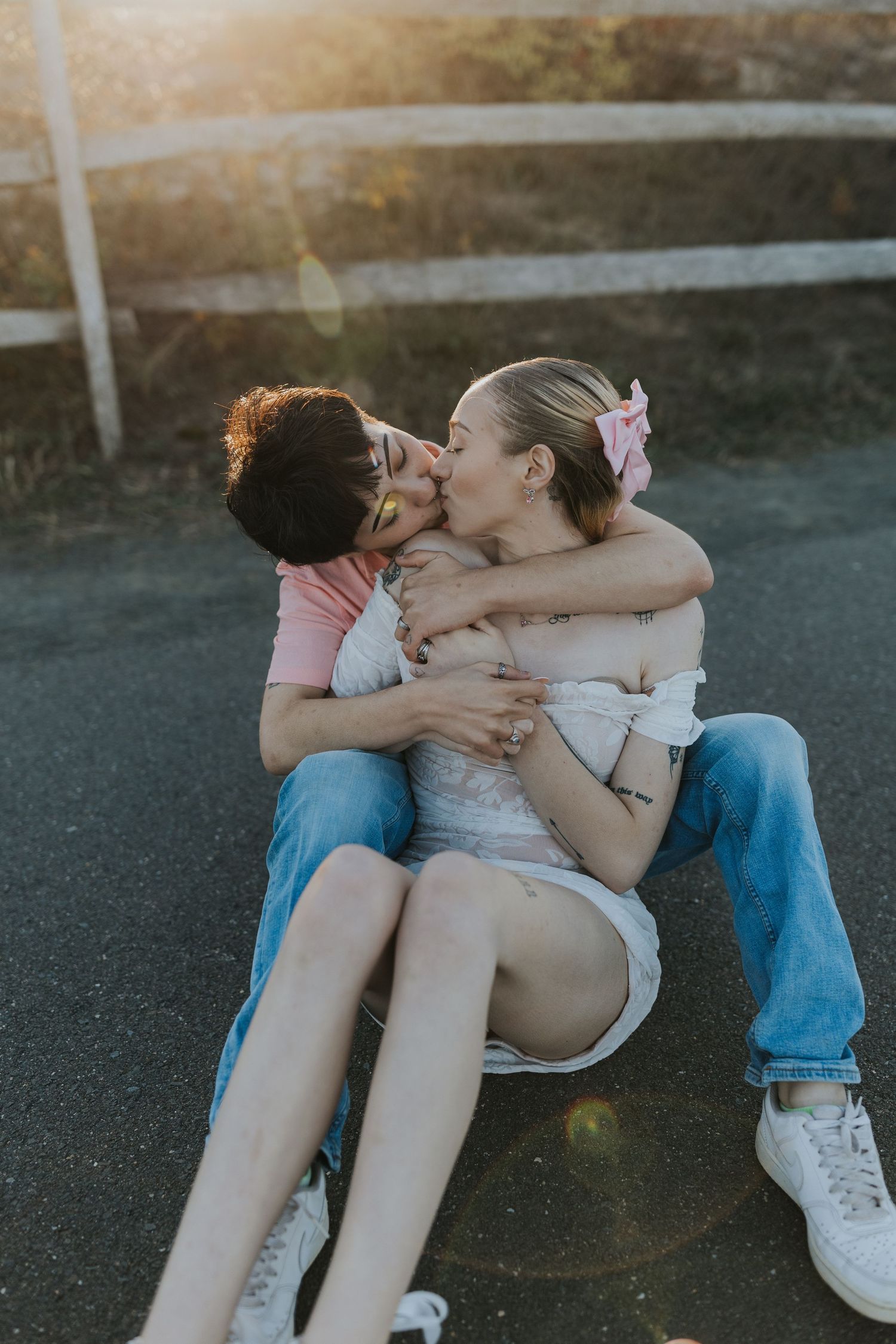 Couple sharing a passionate embrace and kiss while sitting on a road at golden hour.