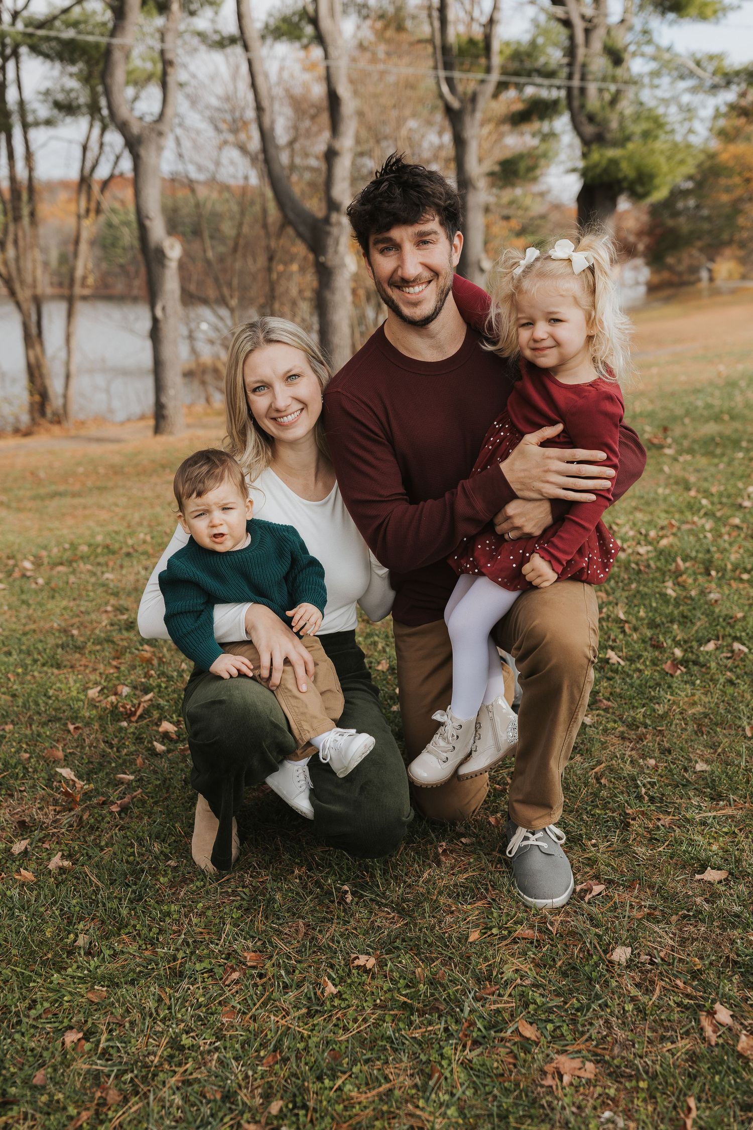 Smiling family of four posing together in a park during a colorful autumn photo session.