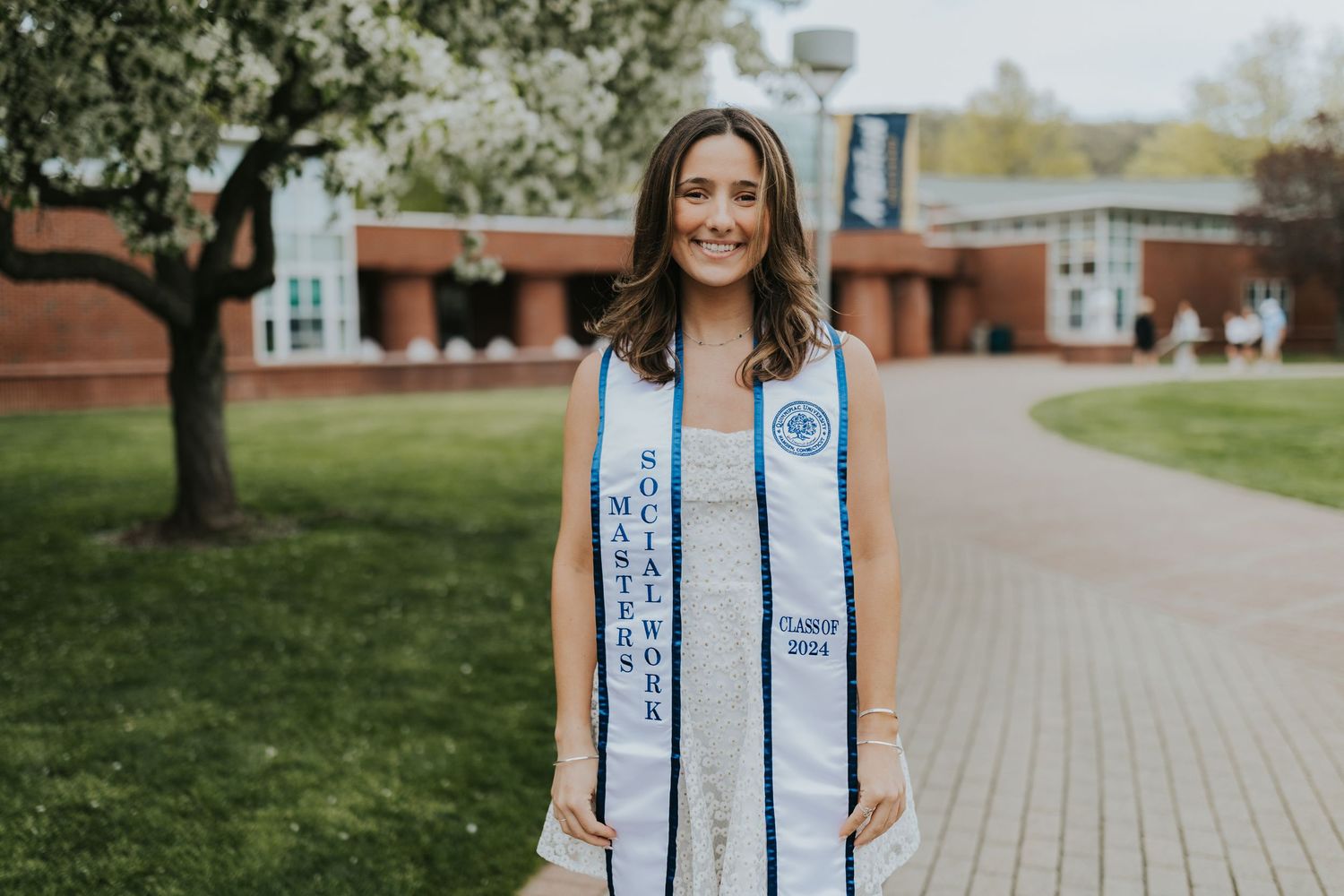 Graduate wearing Masters Social Work Class of 2024 stole smiling on a brick campus walkway.