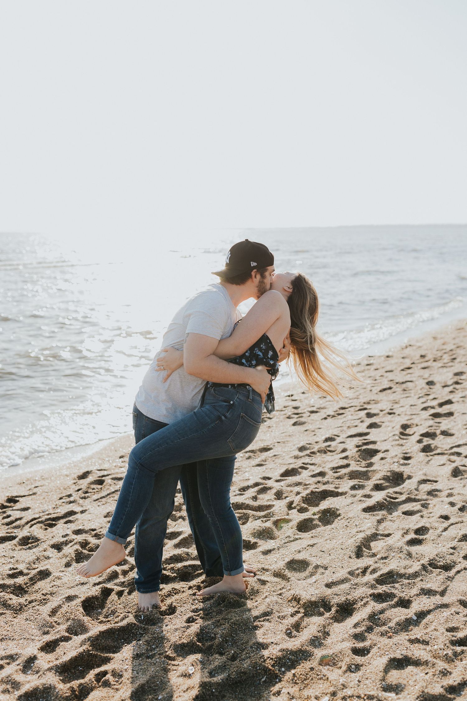 Couple shares a romantic dip kiss embrace on a sandy beach at golden hour sunset.