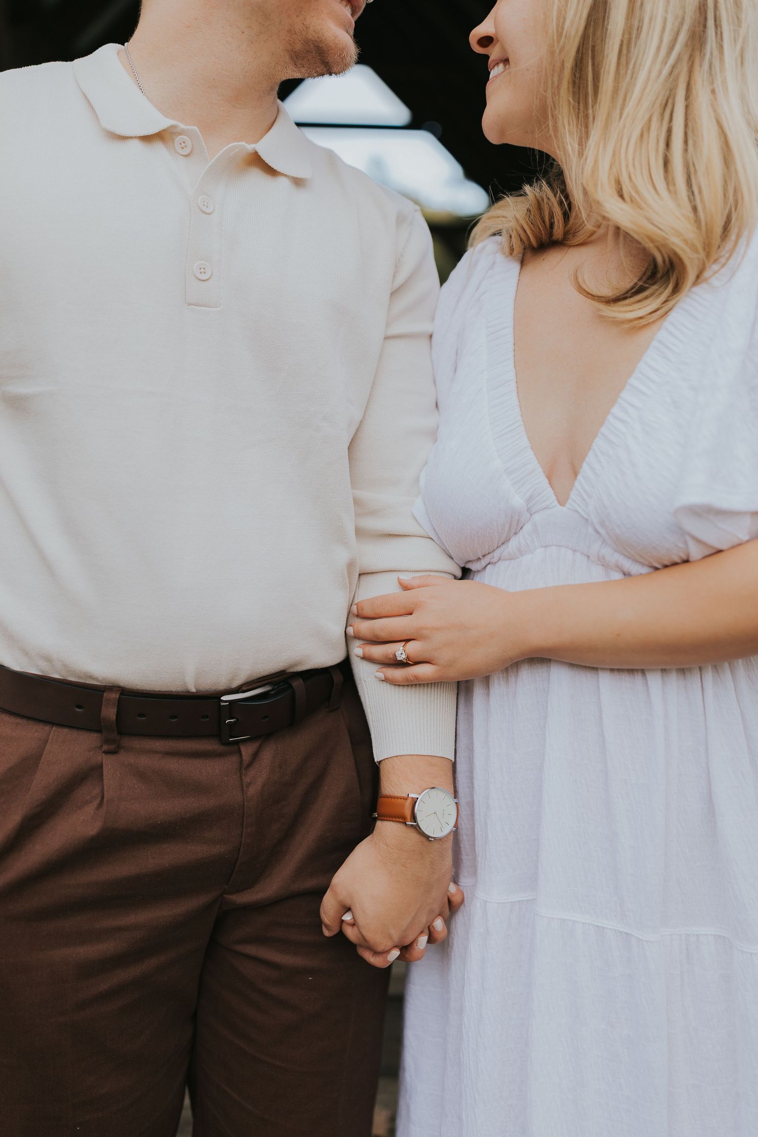 Couple holding hands and smiling at each other in close-up outdoor engagement photo session.