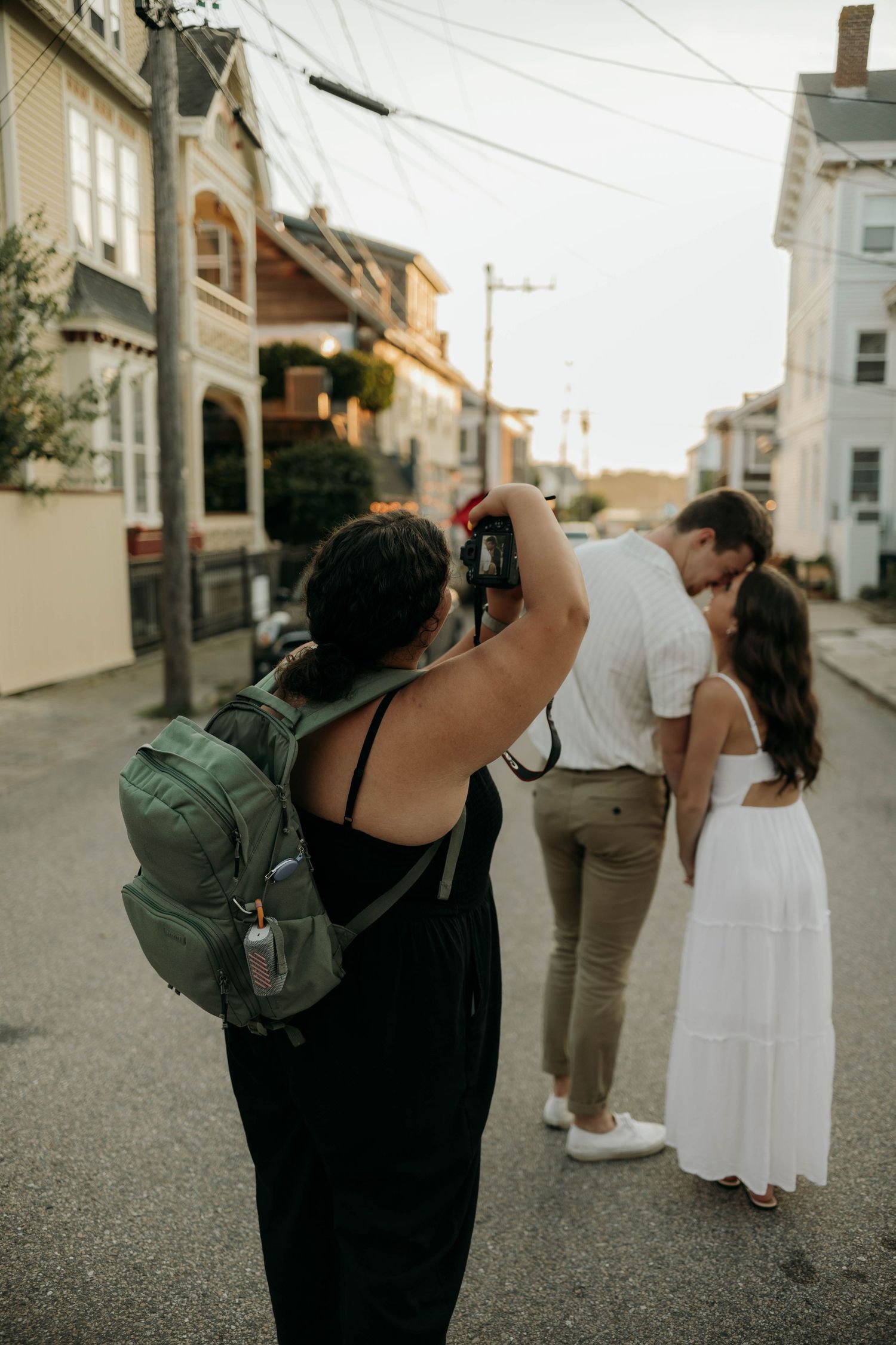 Photographer capturing couple kissing on residential street at golden hour.