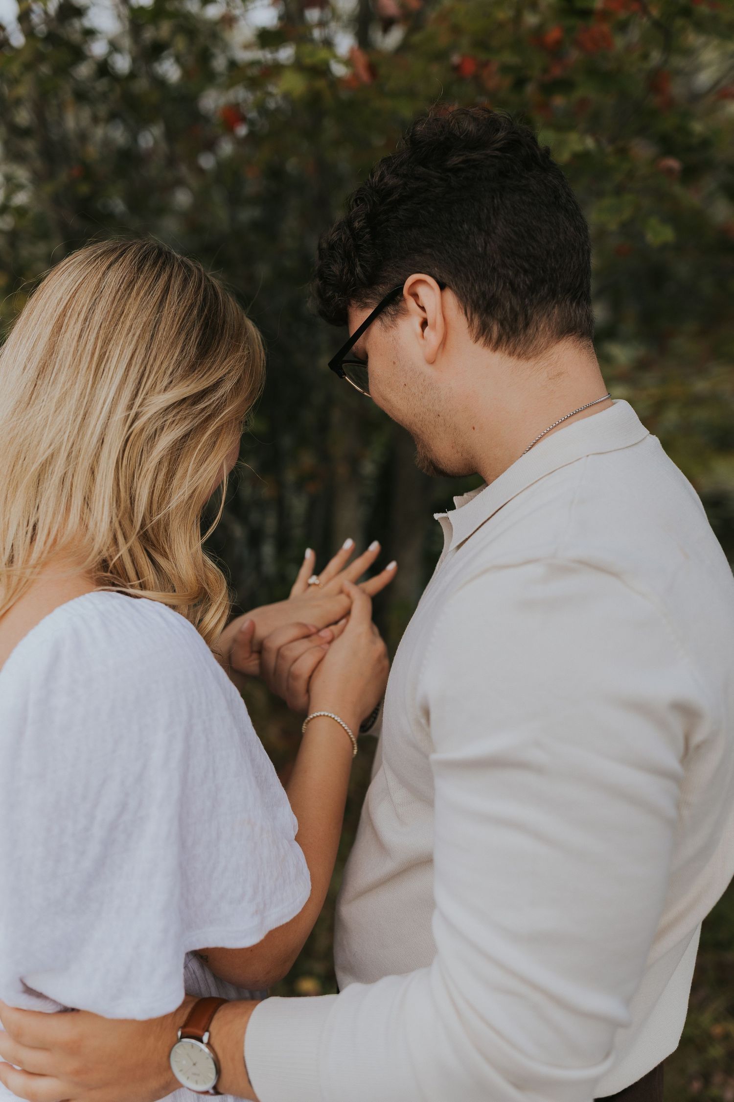 Newly engaged couple admiring engagement ring together outdoors in romantic autumn setting.