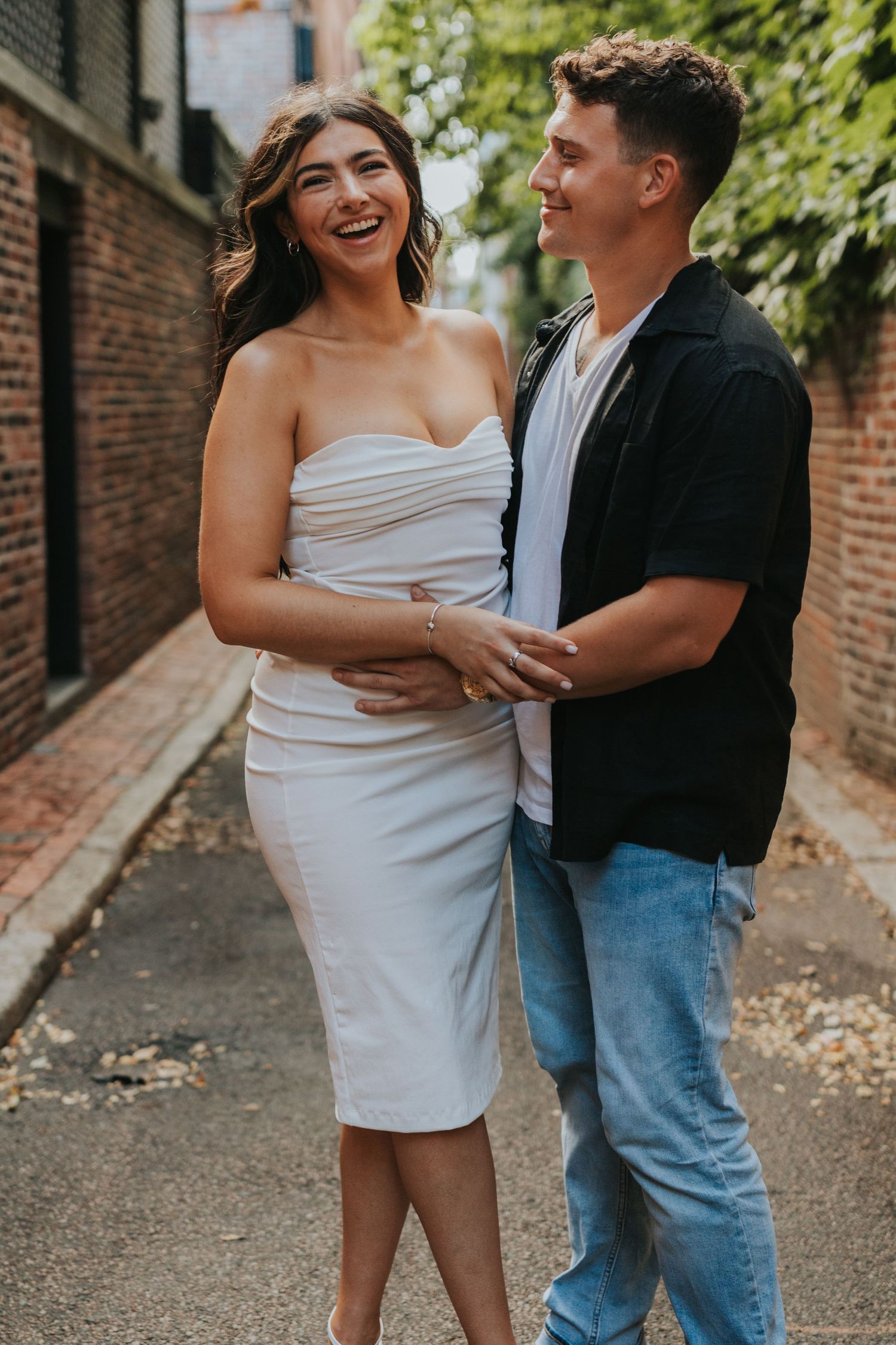 Happy couple laughing and embracing while walking through a charming brick alleyway during engagement session.