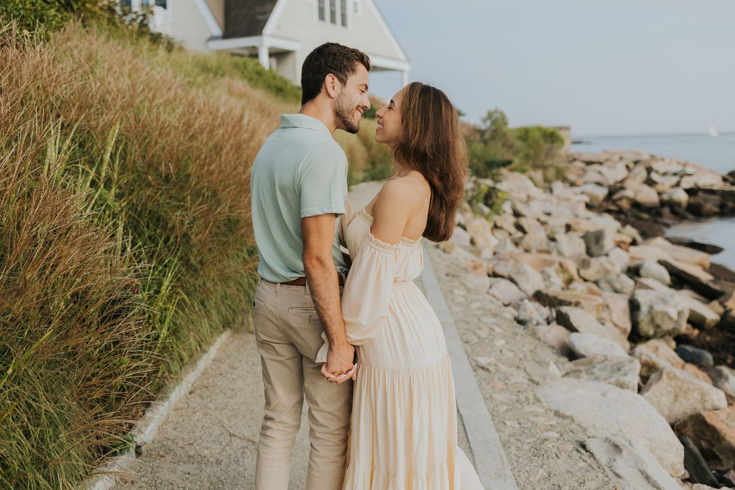 Couple holding hands and sharing a romantic moment on a coastal walkway by the sea.