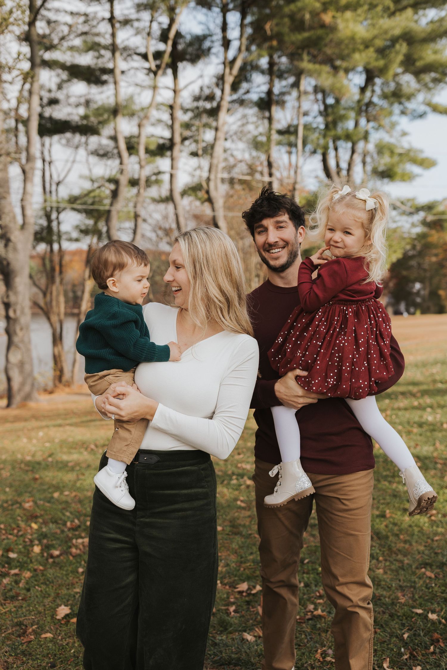 Happy family of four with two young children enjoying a fall day in a tree-lined park.