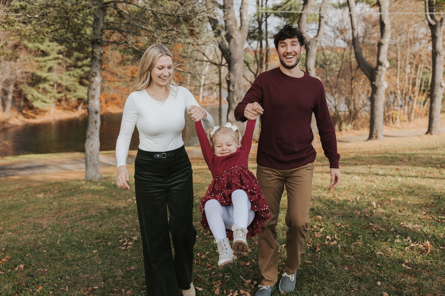 Parents swinging their young daughter between them during a fun autumn family photo session.