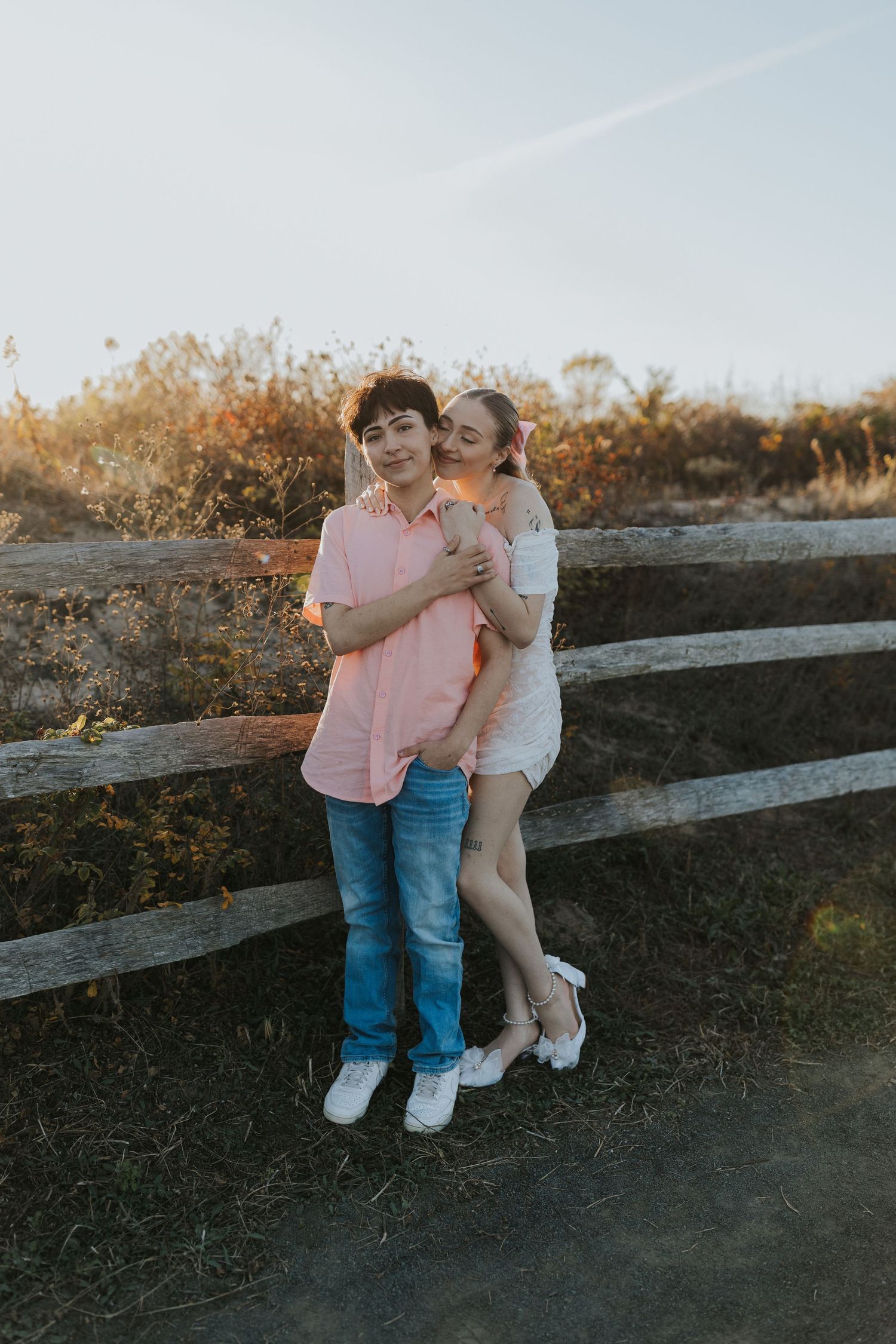Couple posing together by a rustic wooden fence during a warm sunset engagement photo session.