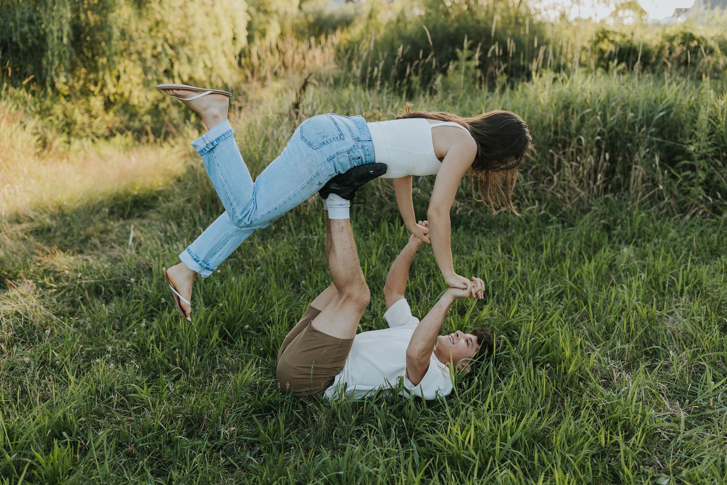 Playful couple doing an acrobatic lift pose together on lush green grass in a sunny park.