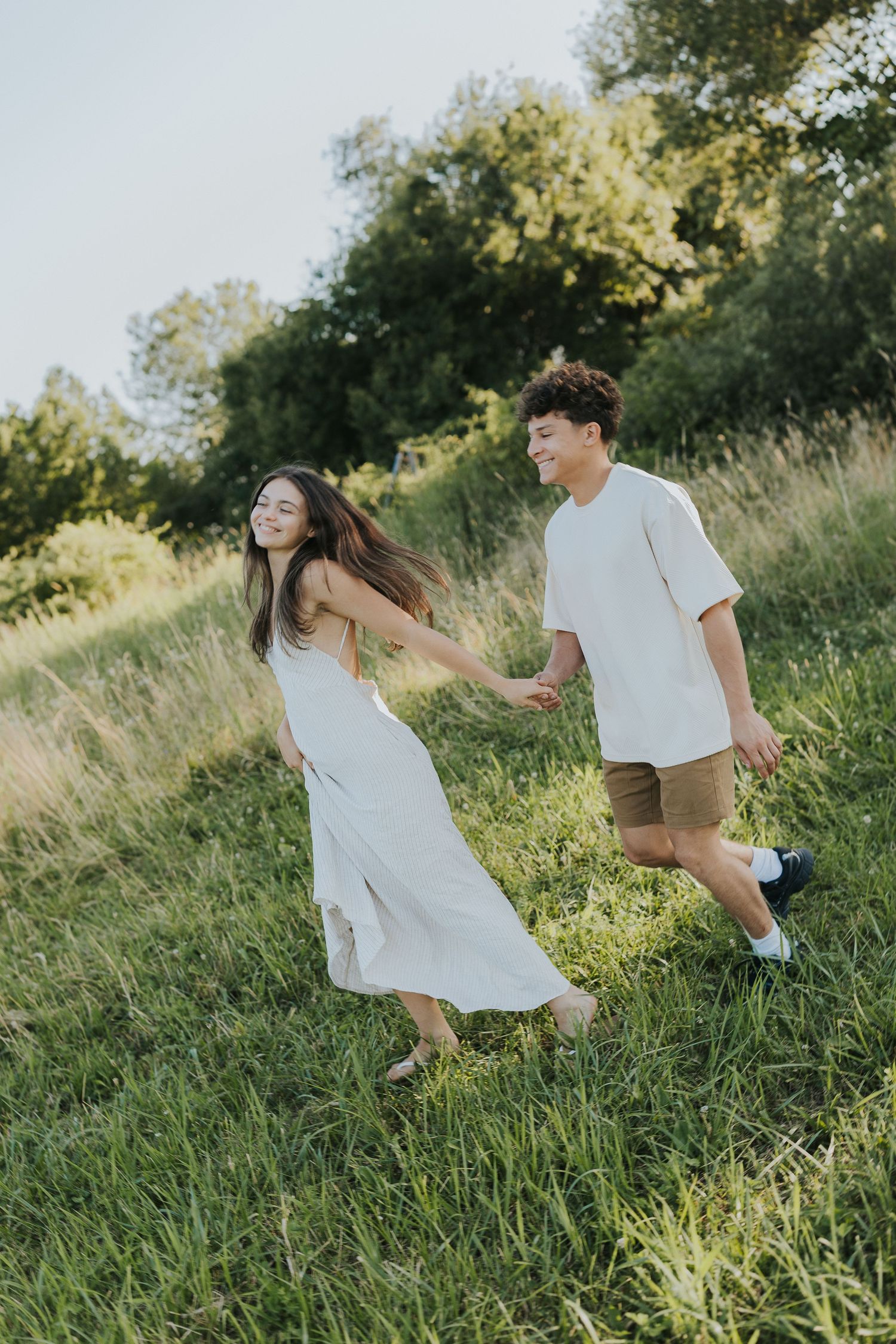 Happy couple holding hands and walking through a sunny green hillside meadow together.