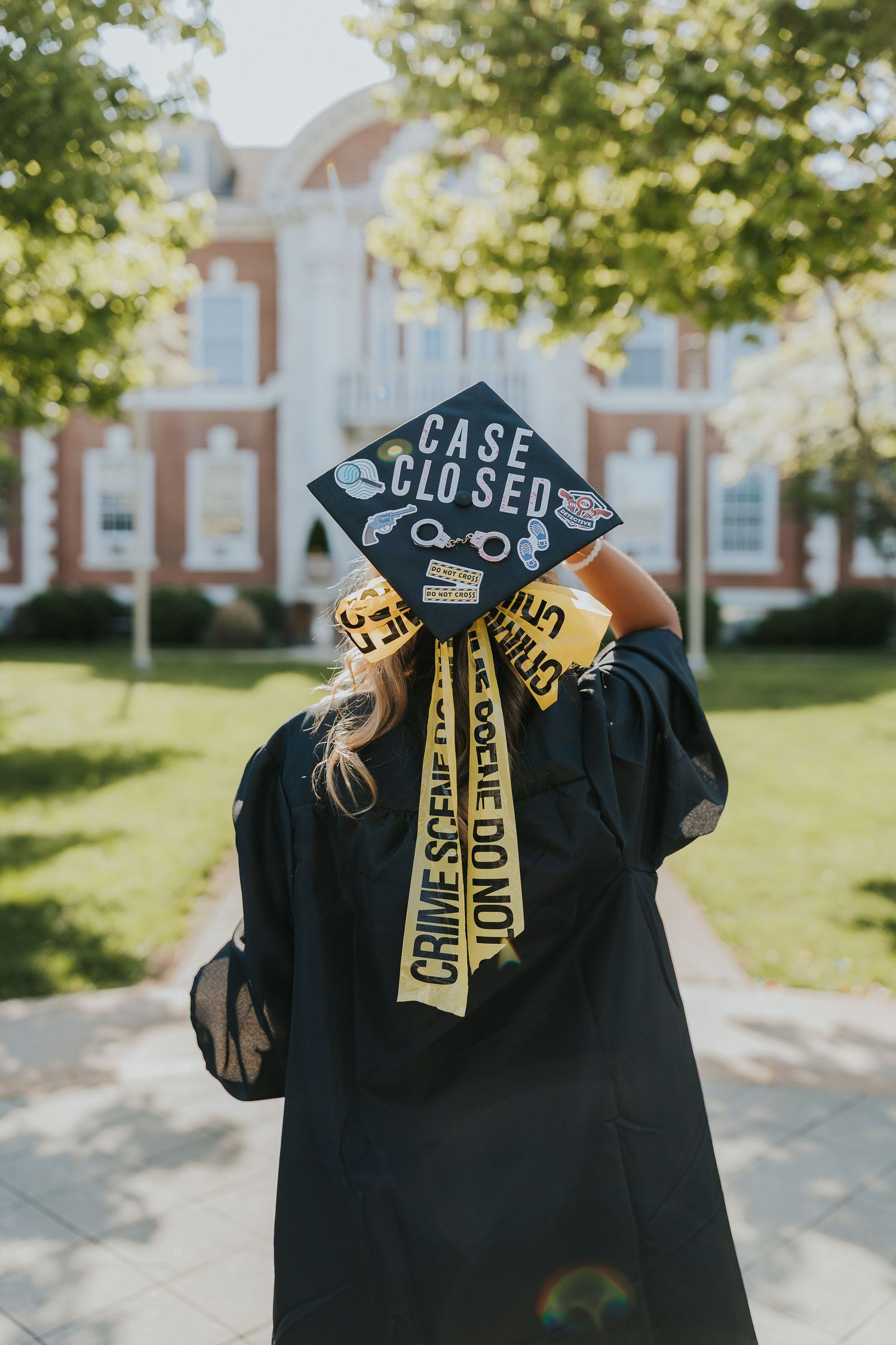 Back view of graduate in black gown displaying Case Closed decorated mortarboard cap with crime scene tape ribbon.