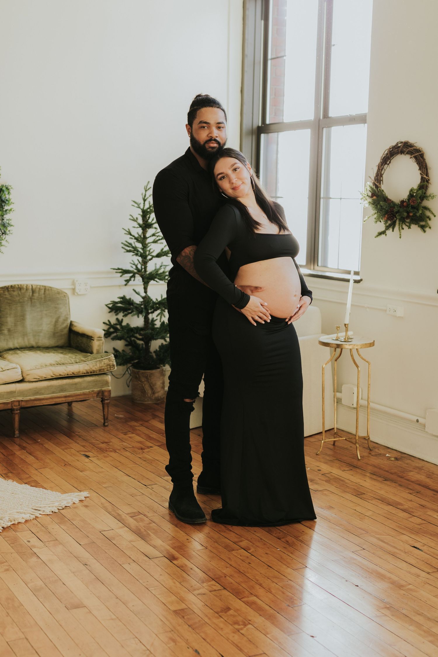Couple in matching black outfits posing together in bright studio with Christmas decor.