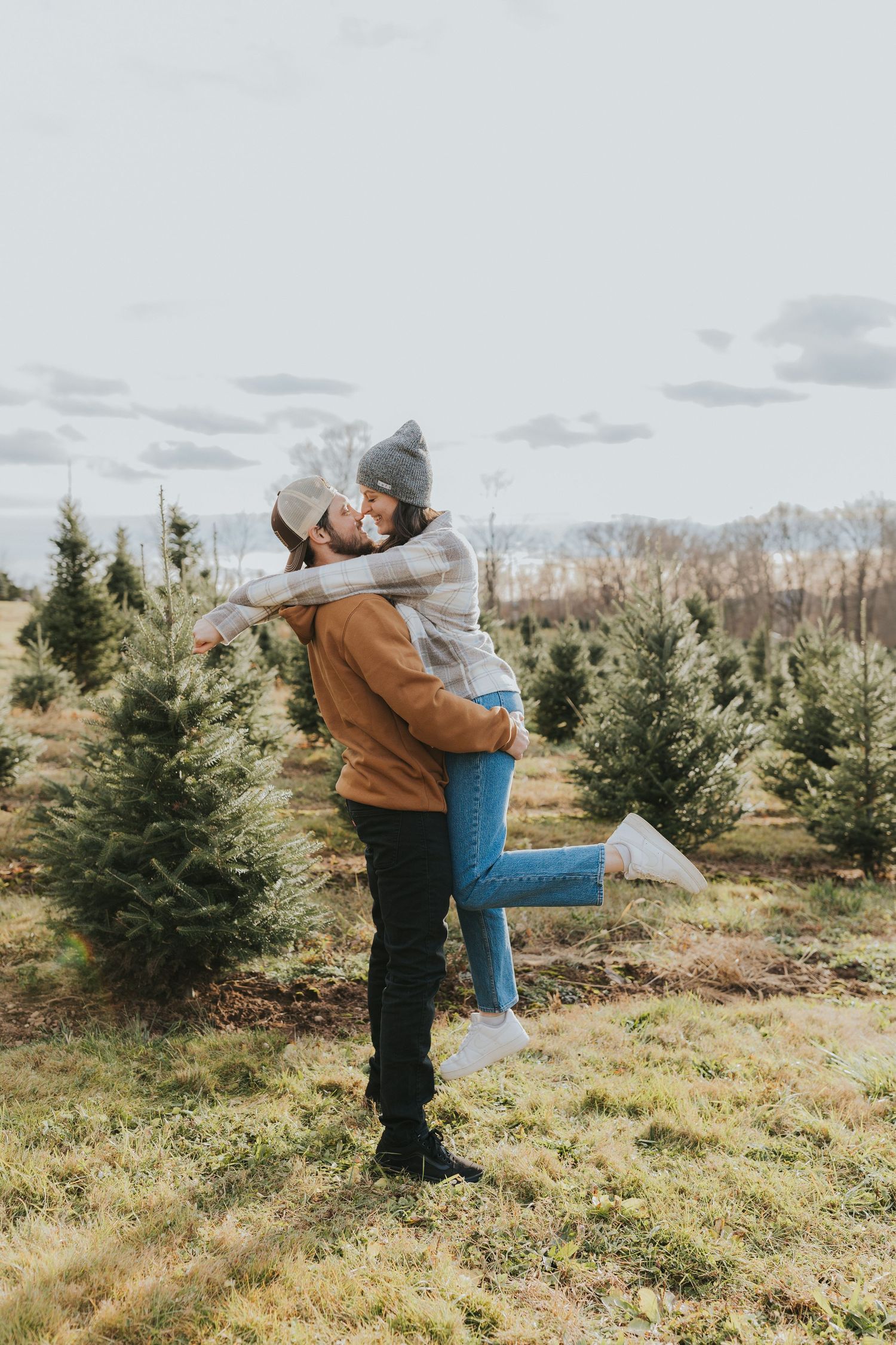 Man lifting woman for a kiss among rows of Christmas trees on a farm.