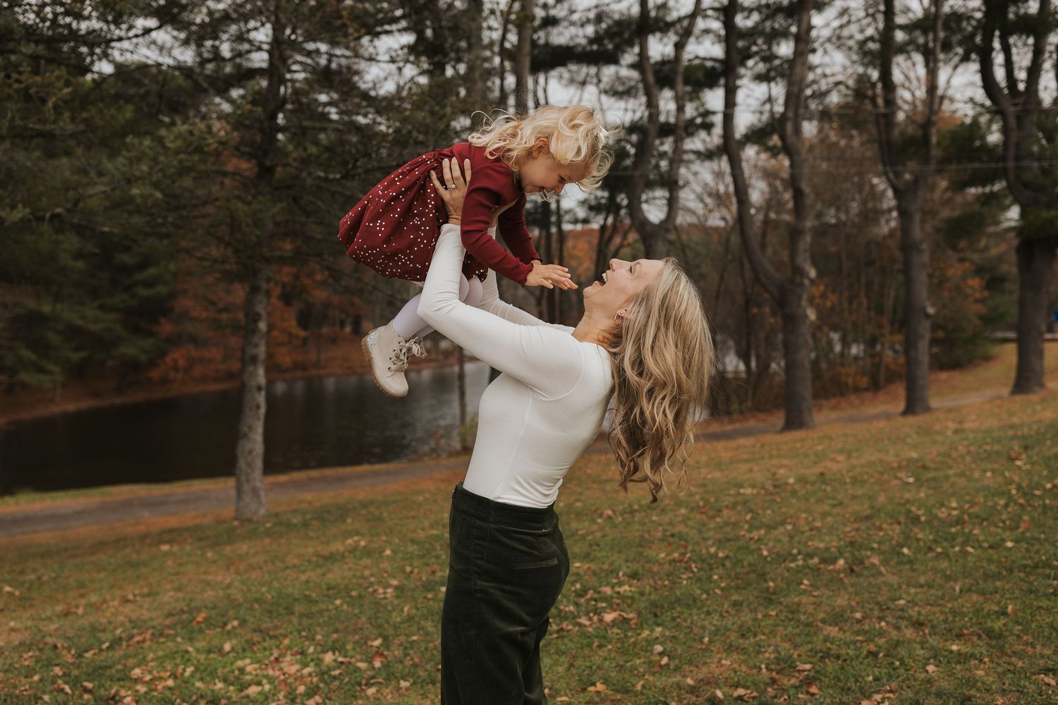 Mother lifting her young daughter in the air during an autumn family photo session in a park.