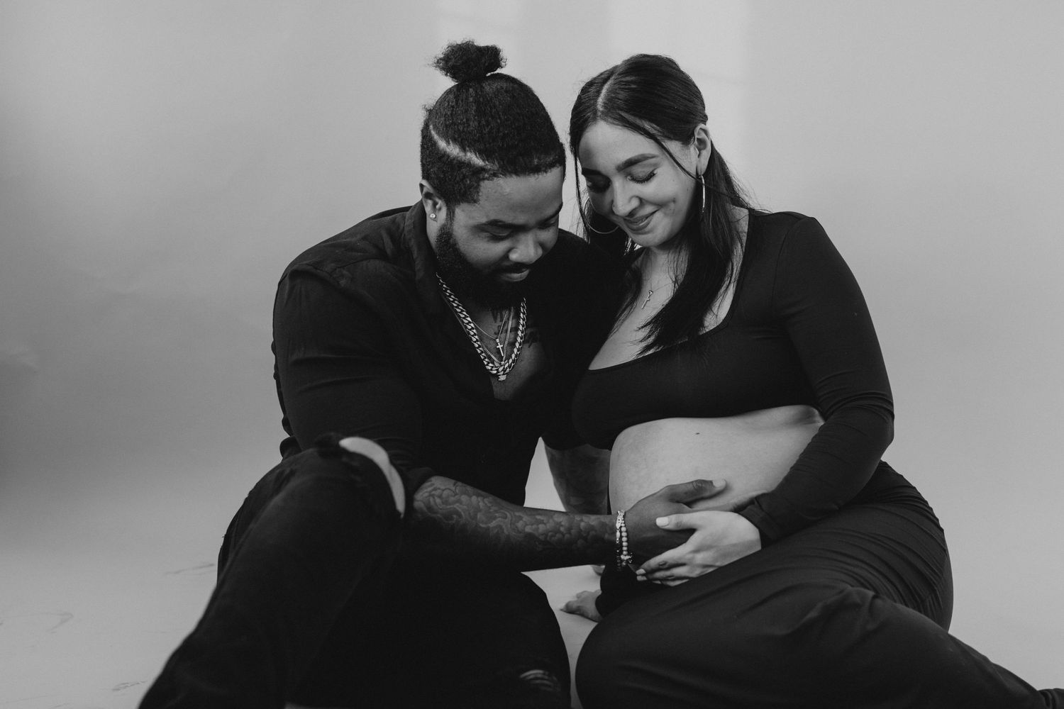 Black and white photo of couple sitting together, man gently touching pregnant woman's belly.