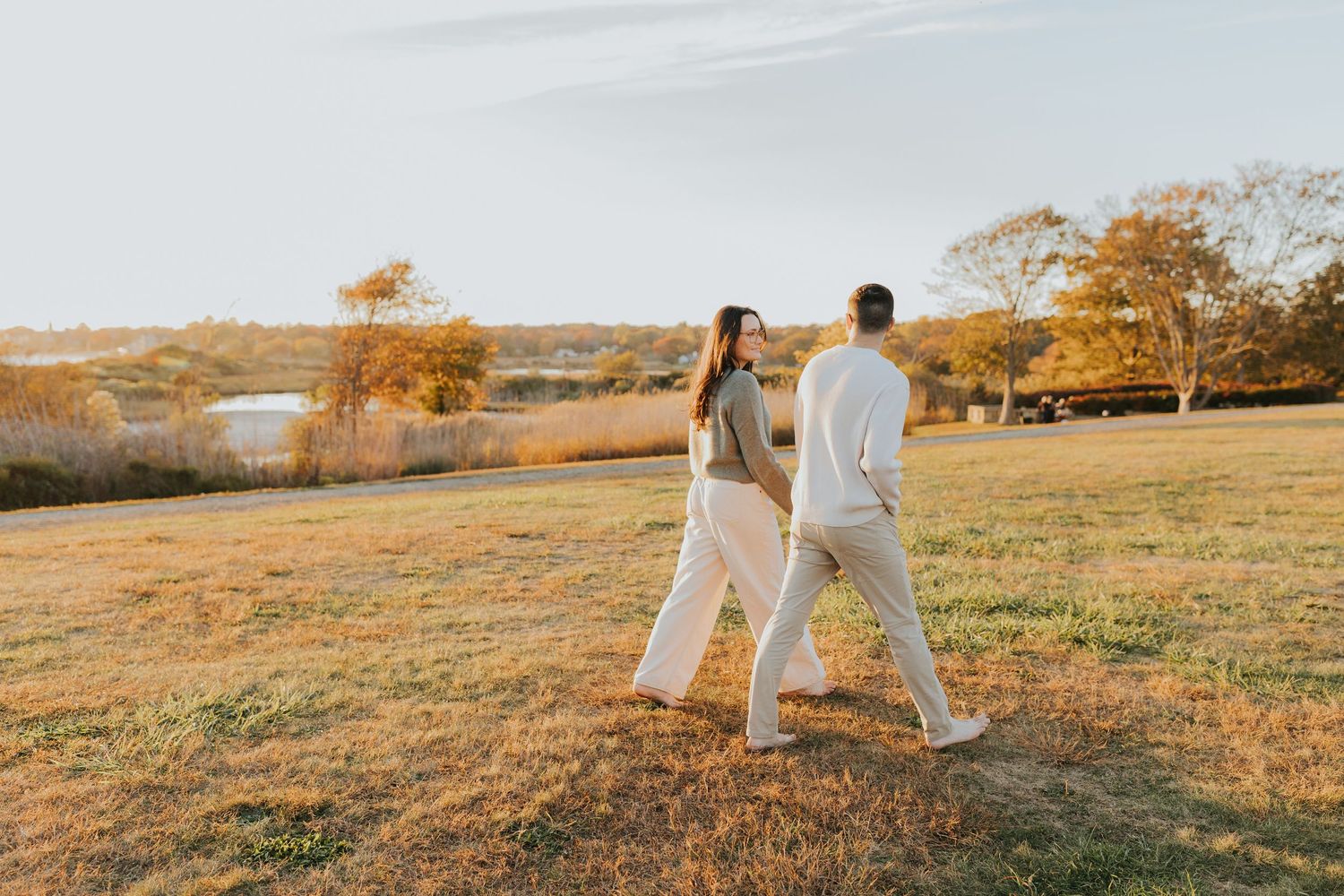 Couple walks together through a golden autumn field during a romantic outdoor engagement session.