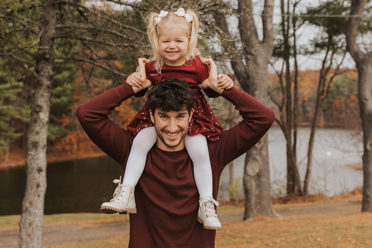 Laughing father carrying his little girl on his shoulders during a fall outdoor photo session.