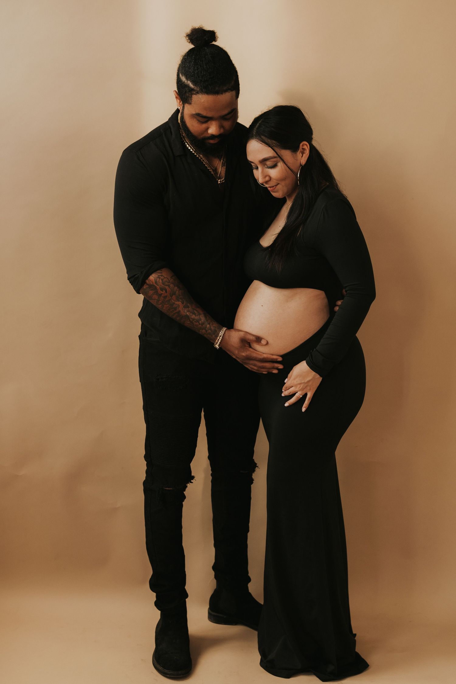 Couple in black outfits tenderly holding pregnant woman's baby bump in studio.