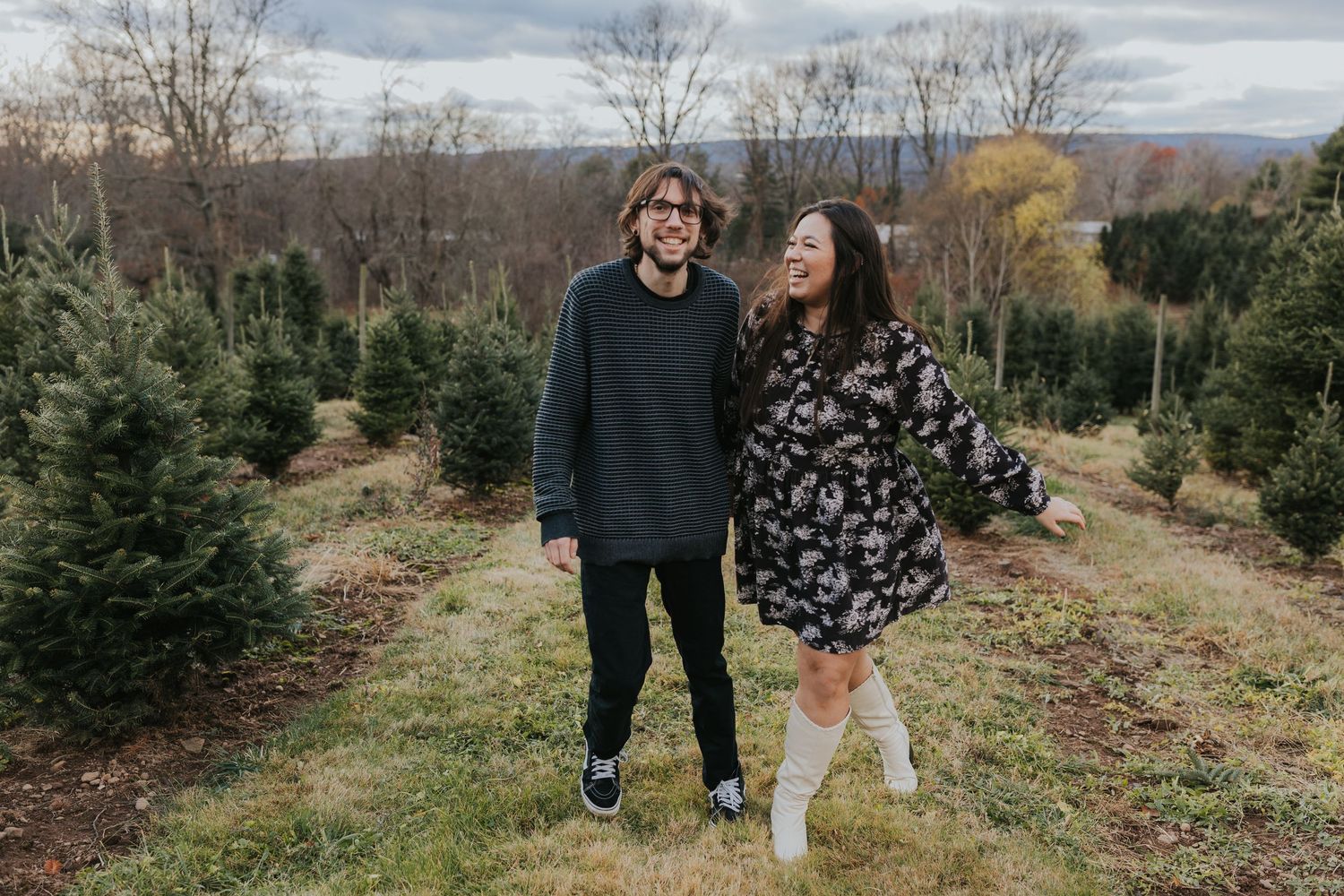 Smiling couple walking together through a Christmas tree farm on a cloudy autumn day.