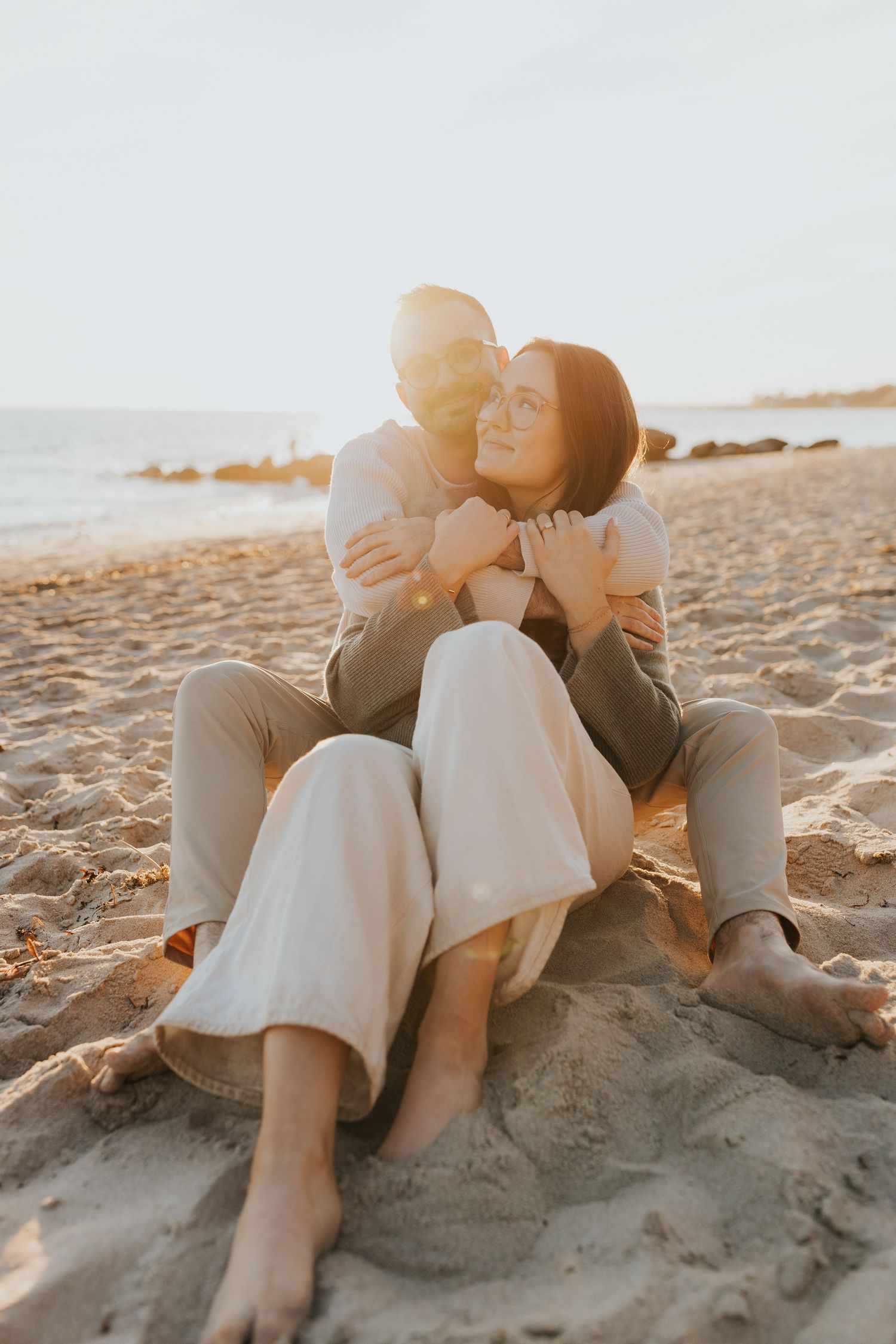 Couple embracing on a sandy beach at golden sunset, sitting together barefoot.