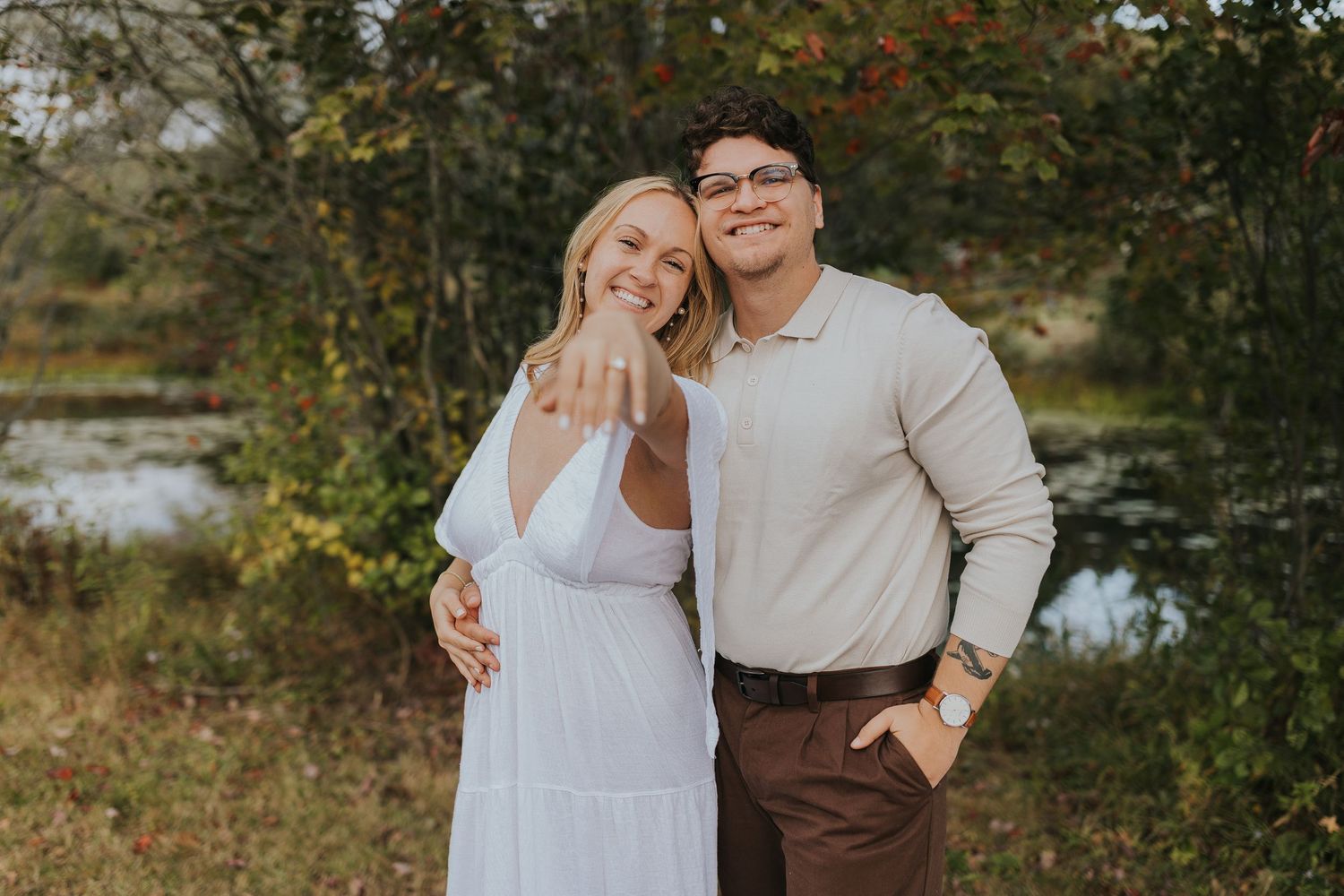 Excited woman showing off engagement ring while posing with fiance outdoors in autumn park.