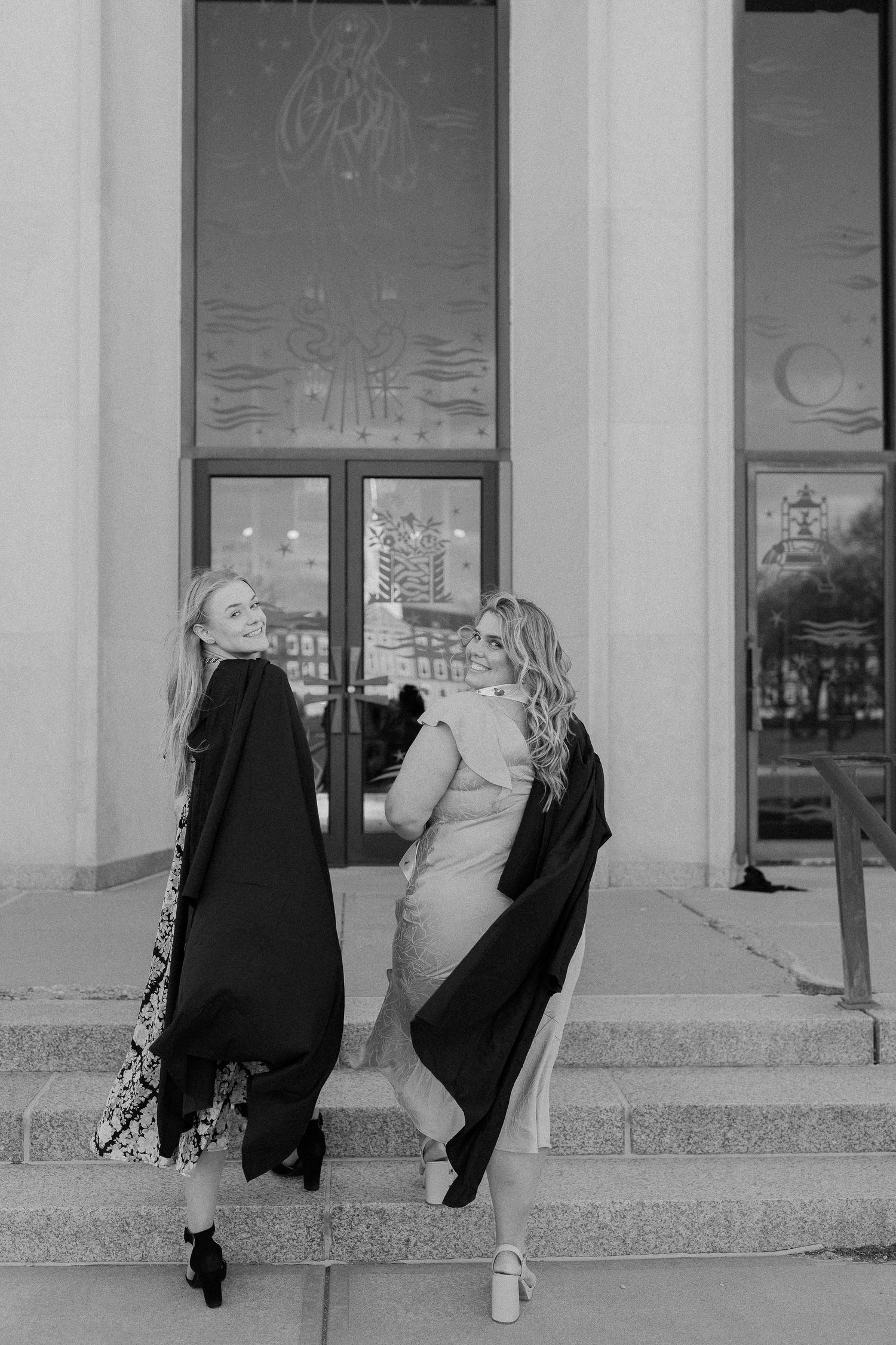 Black and white photo of two graduates in gowns on building steps.